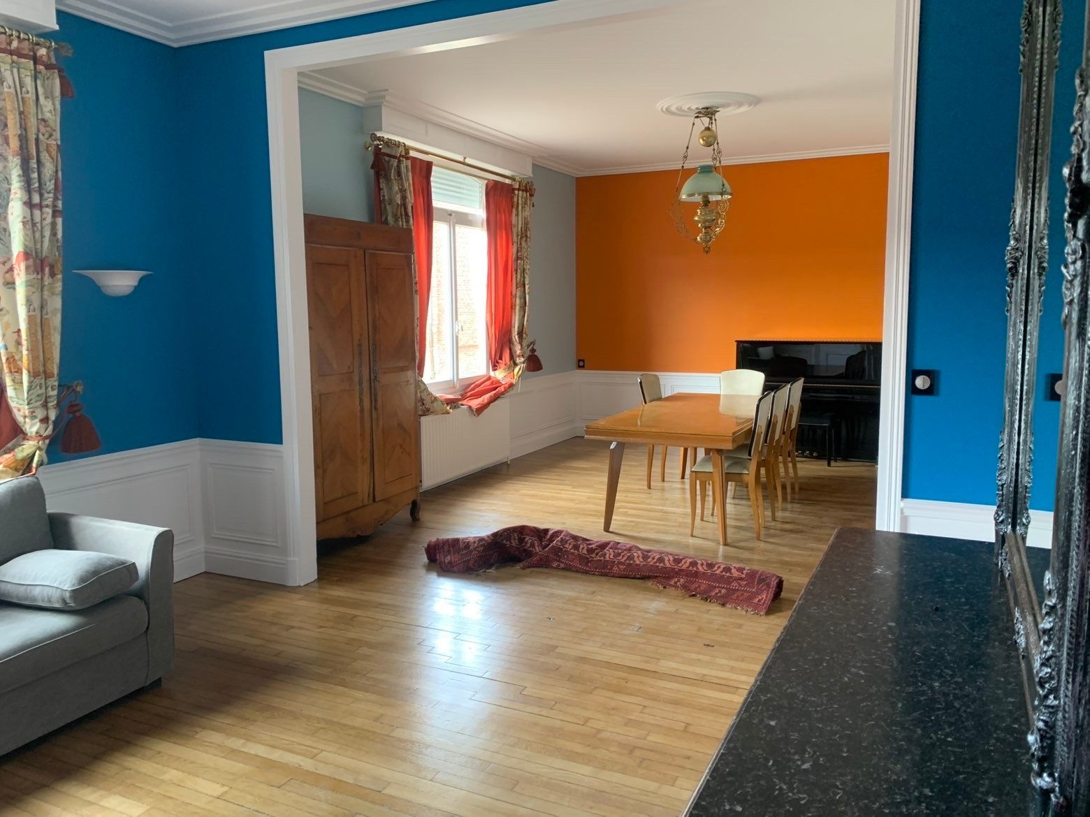 Salon avec murs bleu et orange, meubles en bois et table à manger.