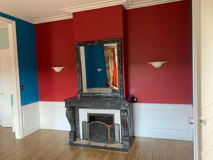 Pièce aux murs rouge et bleu, boiseries blanches, cheminée avec miroir et appliques murales.