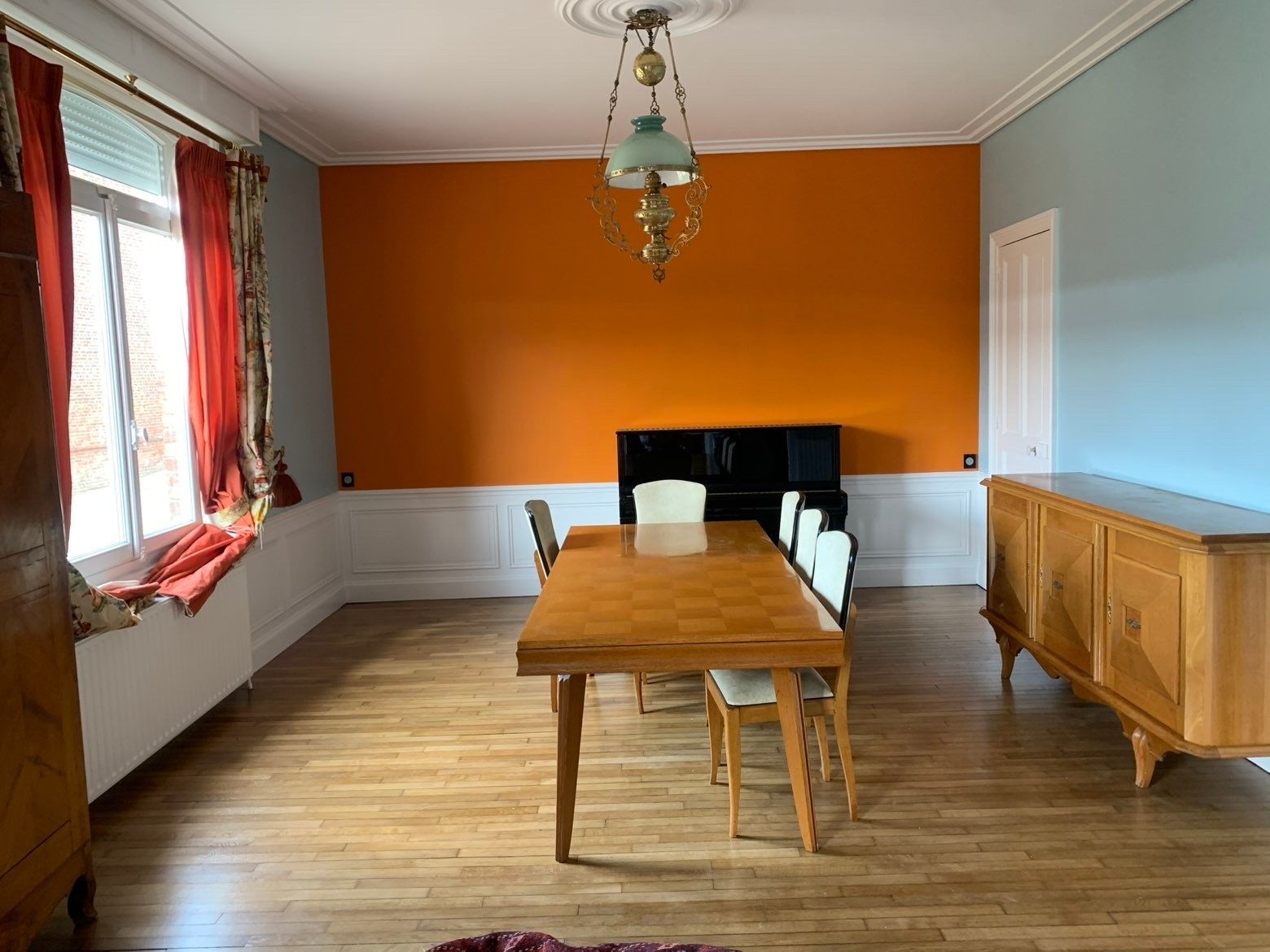 Salle à manger avec table, chaises et buffet en bois. Murs orange et bleu.