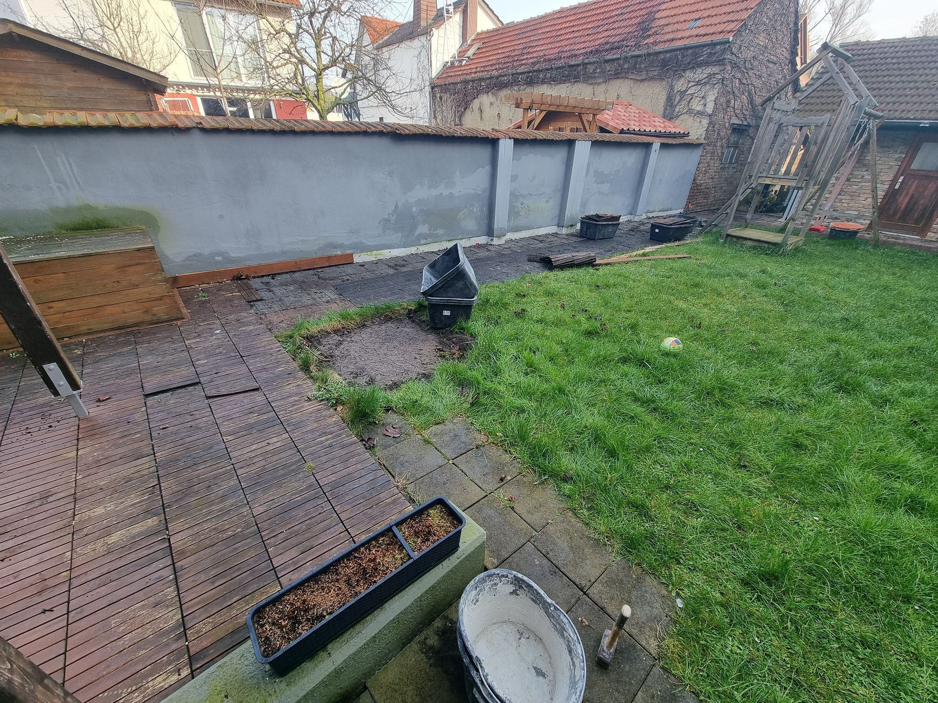 Hinterhofterrasse mit Ziegelpflaster, Rasenfläche, Hochbeeten und einem kleinen schwarzen Grill am Zaun
