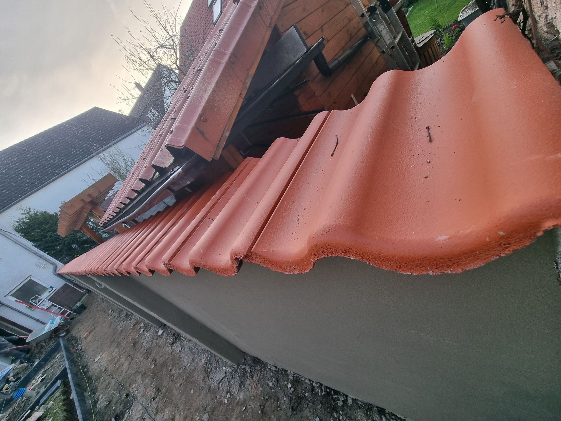 Schrägansicht eines Terrakotta-Dachs mit gewellten Ziegeln neben einem Haus und Hof