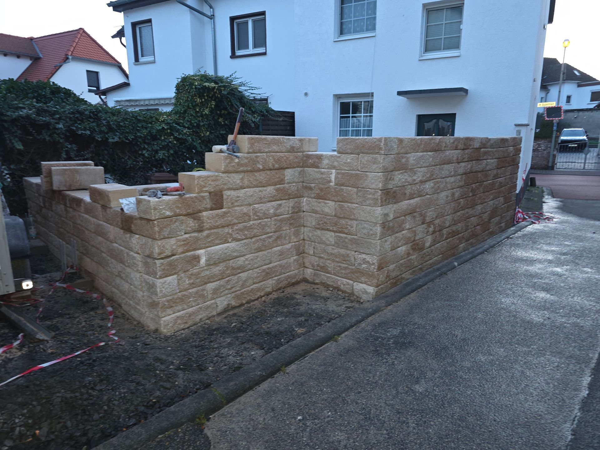 Eine im Bau befindliche Steinstützmauer neben einem Haus in einer feuchten Wohnstraße