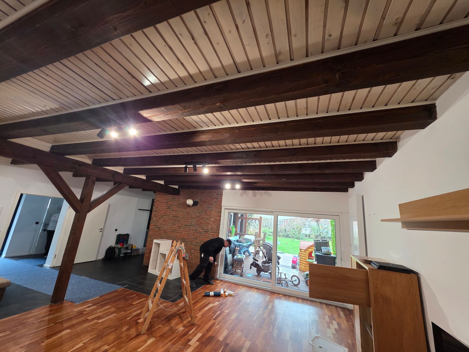 Innenbereich mit Holzbalkendecke, Person in Fensternähe, Holzböden.