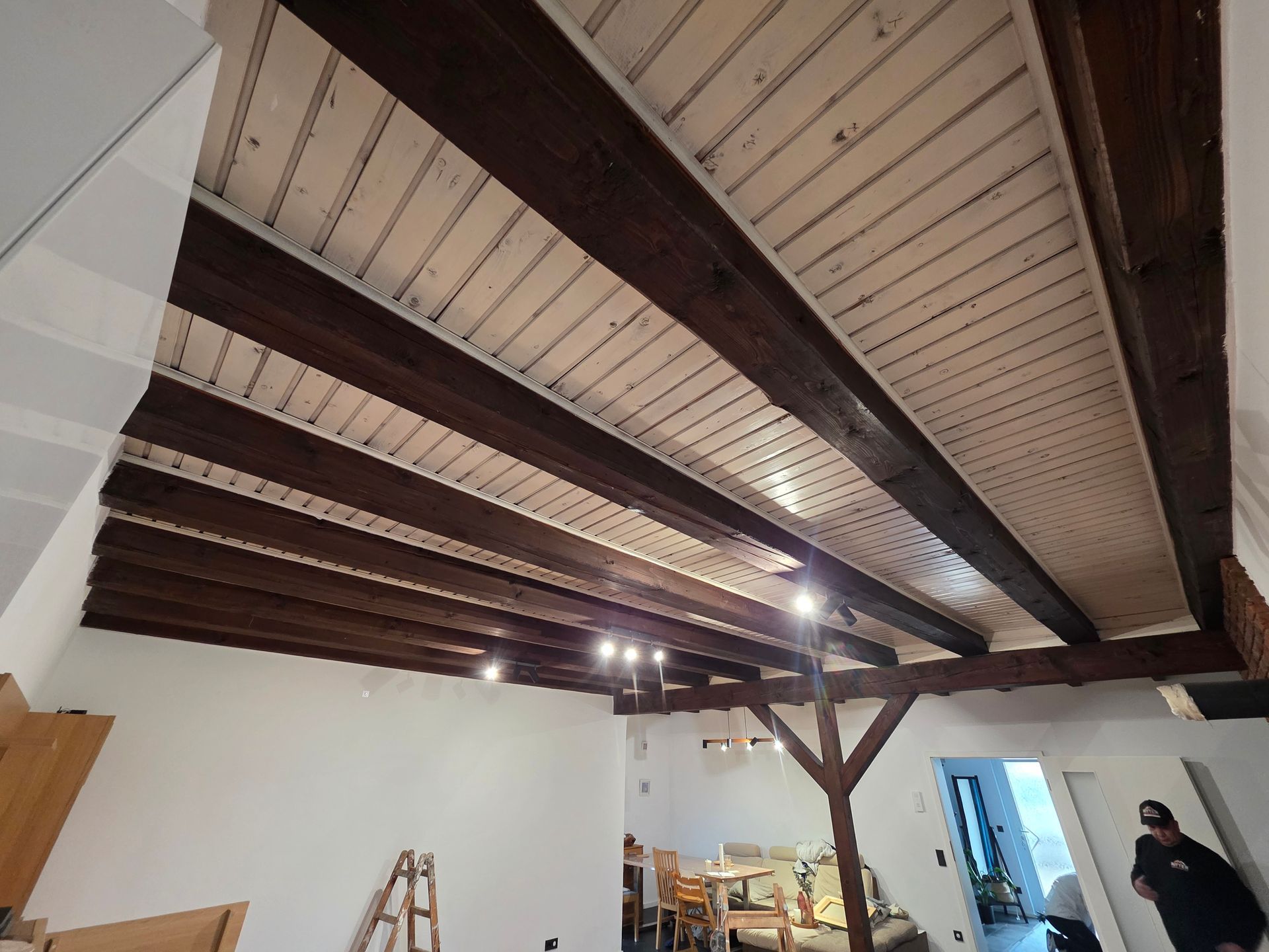 Holzdecke mit dunklen Balken und weißen Paneelen, Zimmer mit Beleuchtungskörpern.