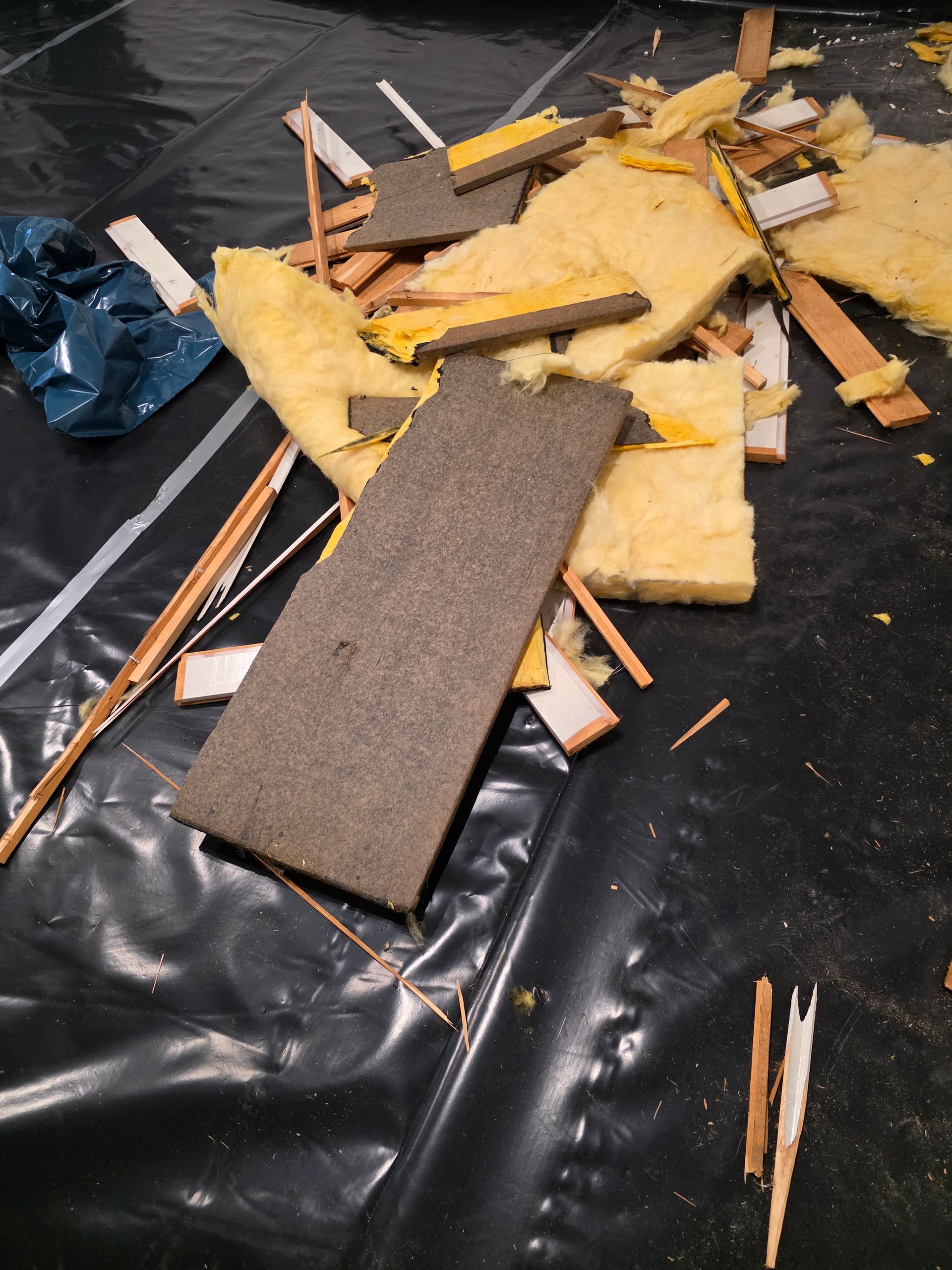 Haufen von Bauschutt auf schwarzer Plastikfolie, darunter Dämmmaterial und Holz.