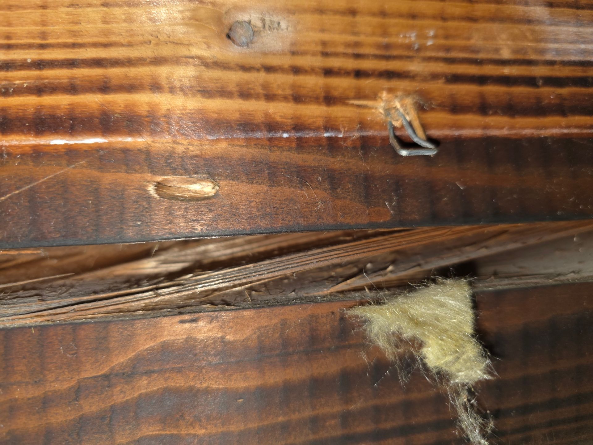 Holzbalken mit Isolierung und Metallklammer; Nahaufnahme zeigt Beschädigungen und Abnutzungsspuren.