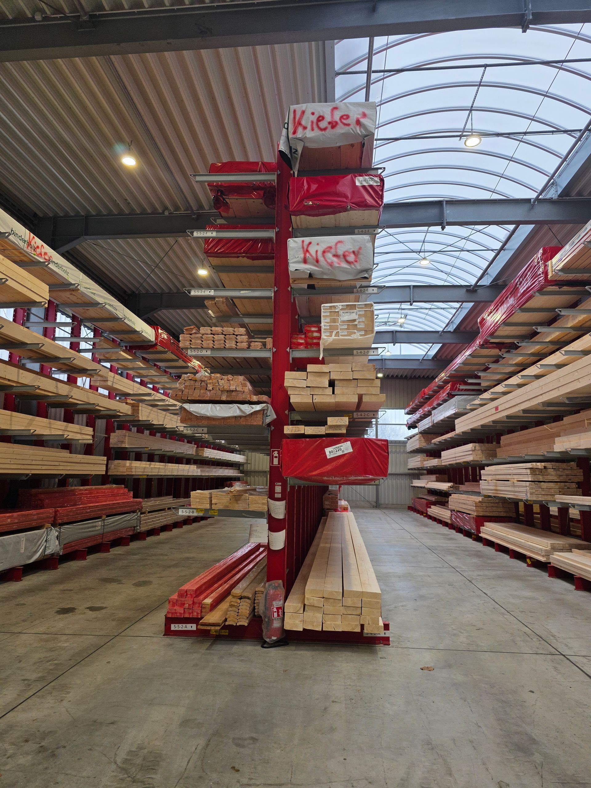 Innenansicht einer Lagerhalle mit Reihen von Holzbrettern auf roten Regalen.