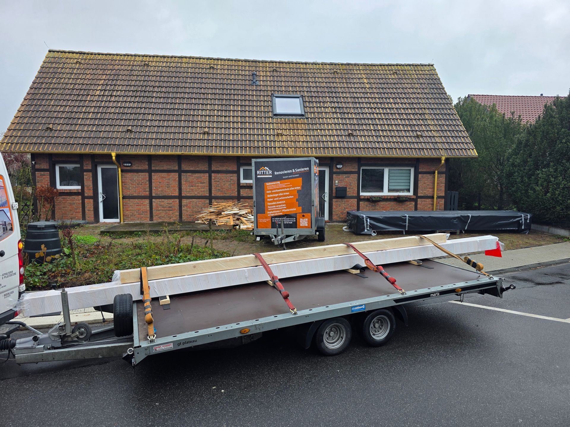 Anhänger mit Balken vor einem Haus, das renoviert wird.