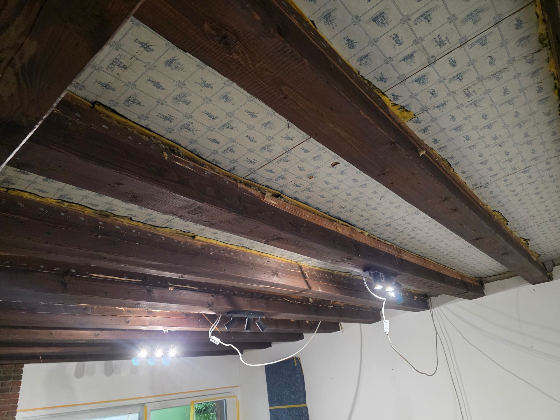 An der Decke sind Holzbalken mit Dämmplatten angebracht, die elektrische Verkabelung ist sichtbar.