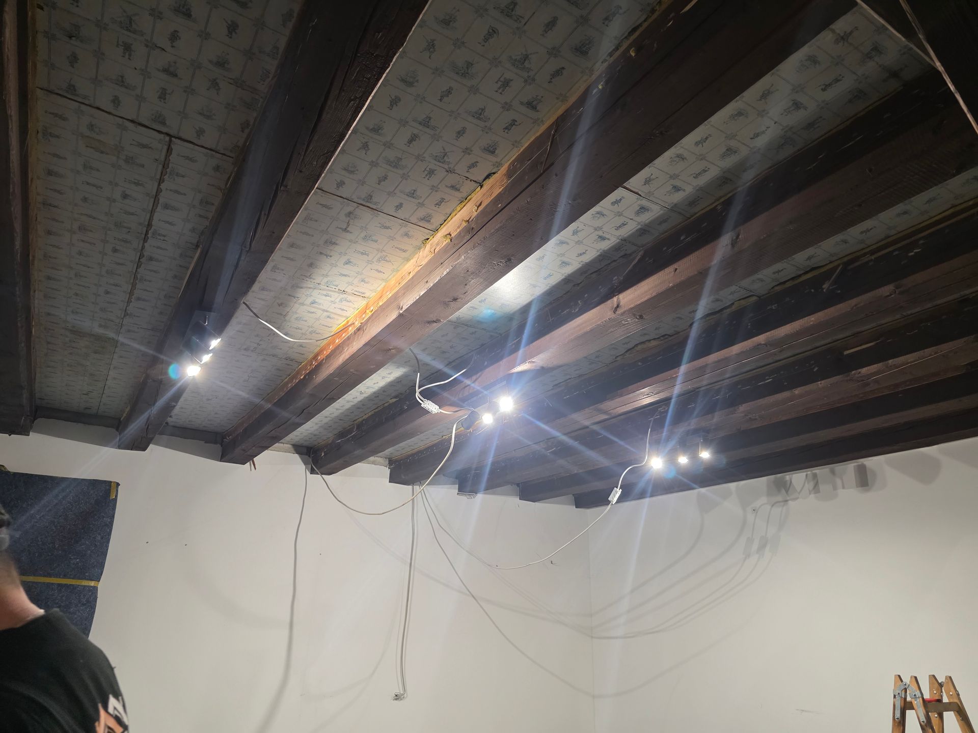 Decke mit sichtbaren Holzbalken, installierter Beleuchtung und Verkabelung. 