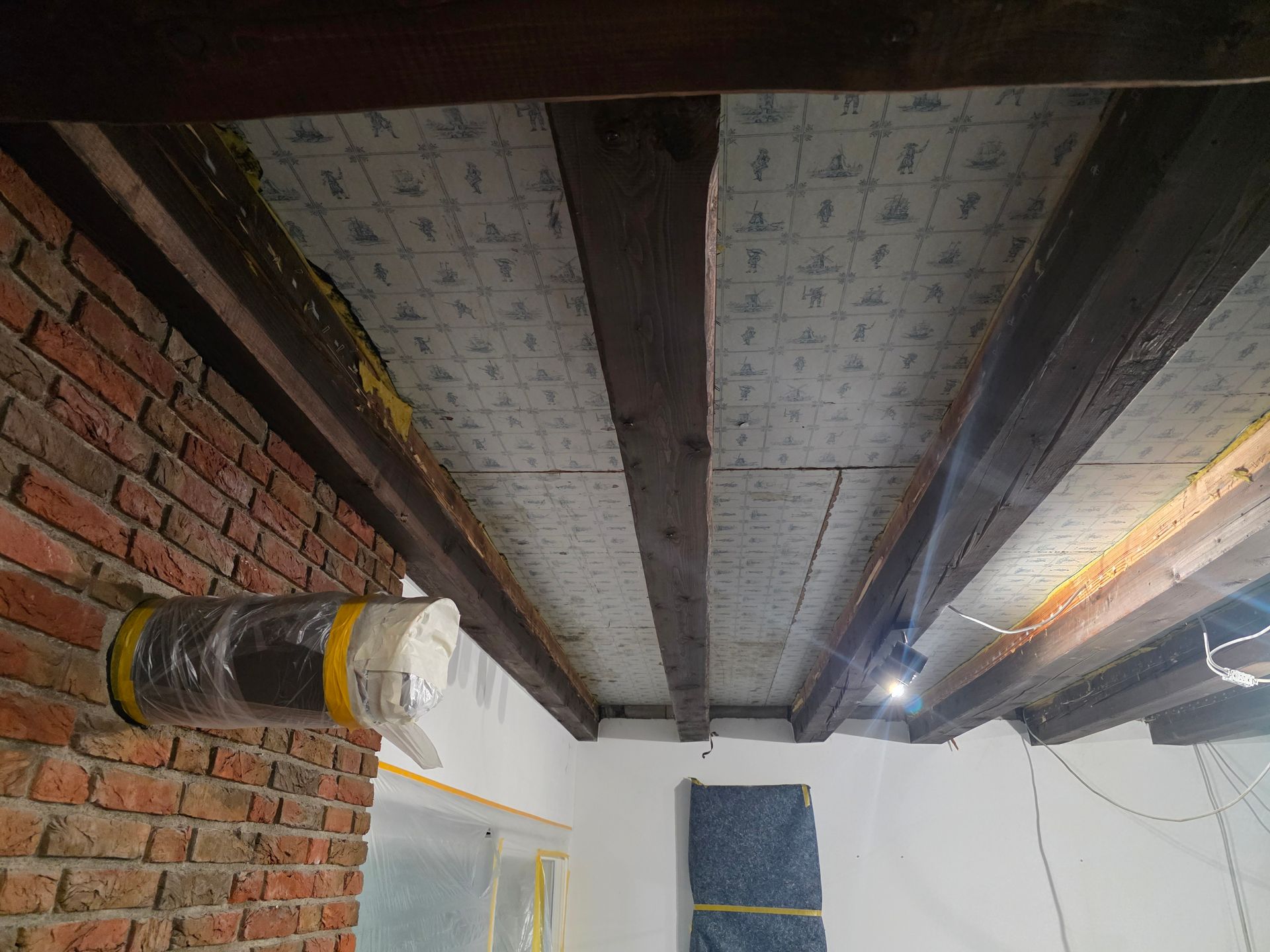 Sichtbare Deckenbalken mit Dämmplatten, Ziegelwand und Lüftungskanälen.