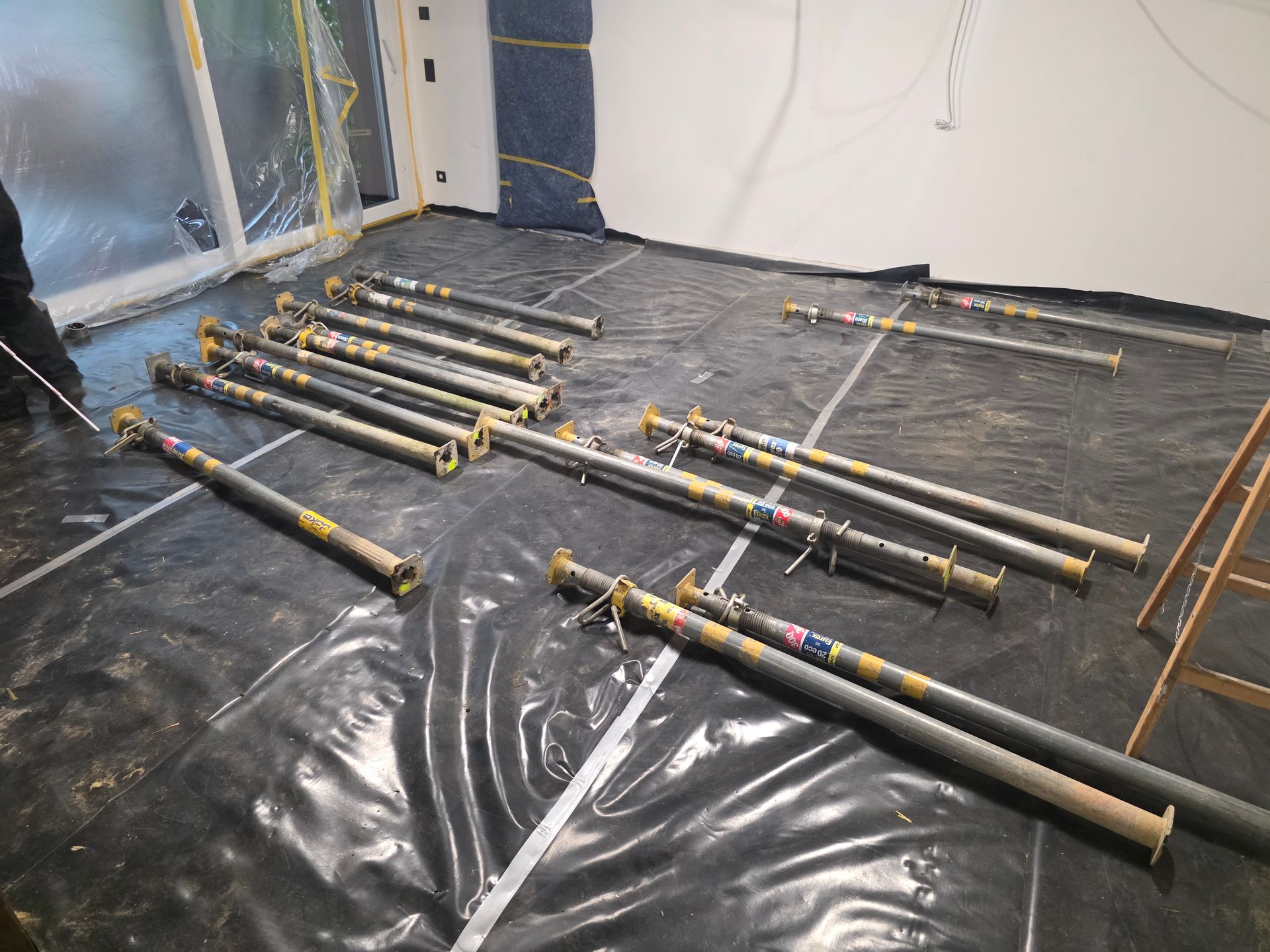 Metallstützbalken liegen in einem Raum in der Nähe eines Fensters auf schwarzer Plastikfolie.