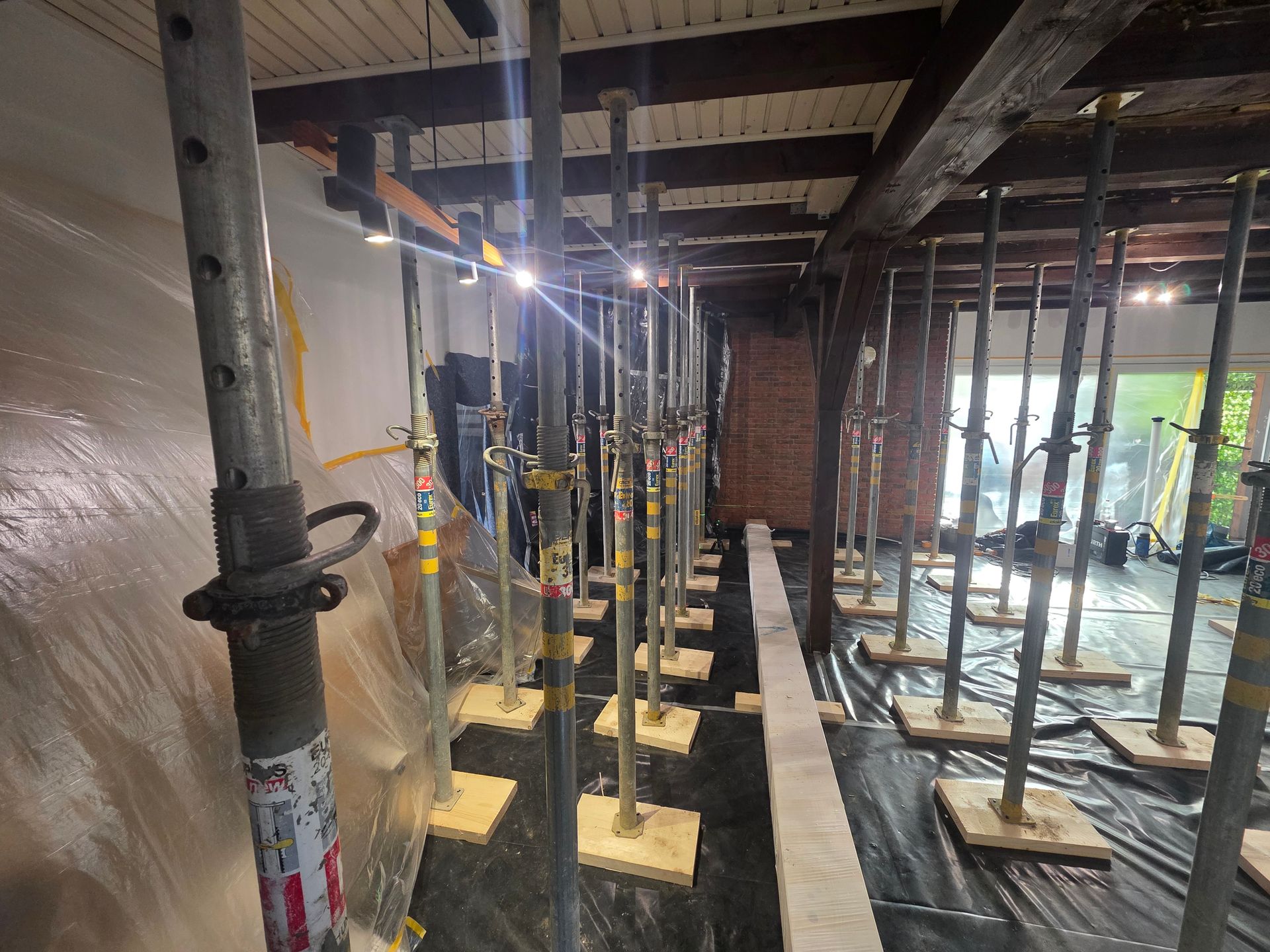 Innenansicht einer Baustelle mit Stützpfeilern. Dunkle Decke, Plastikfolie und Ziegelwand.