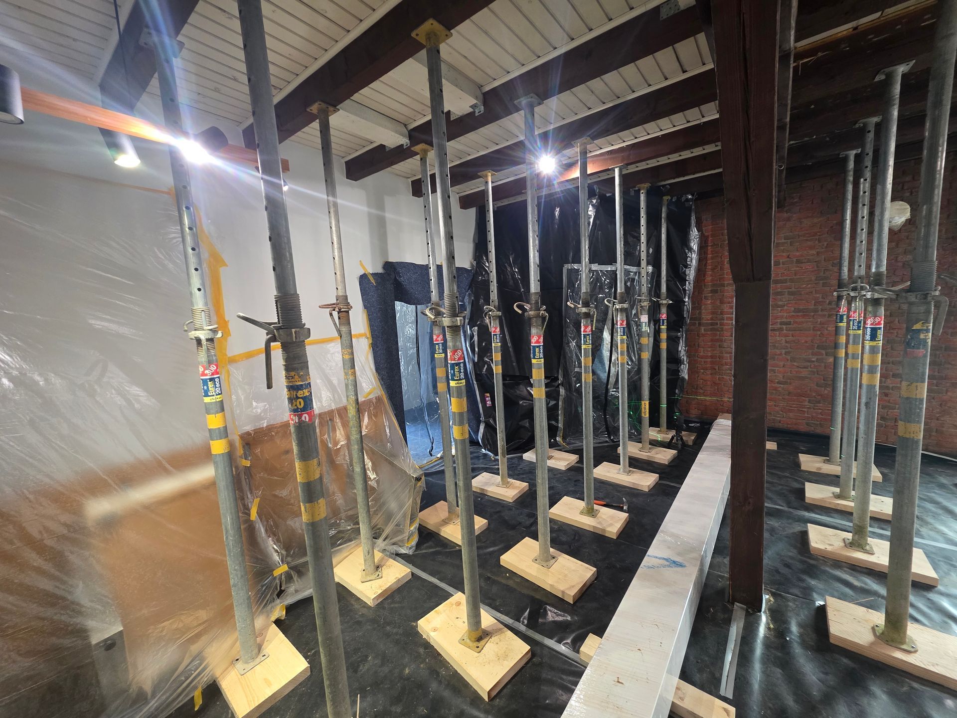 Reihen von verstellbaren Metallstützpfosten in einem Raum, die auf Holzsockeln unter einer Decke angebracht sind.