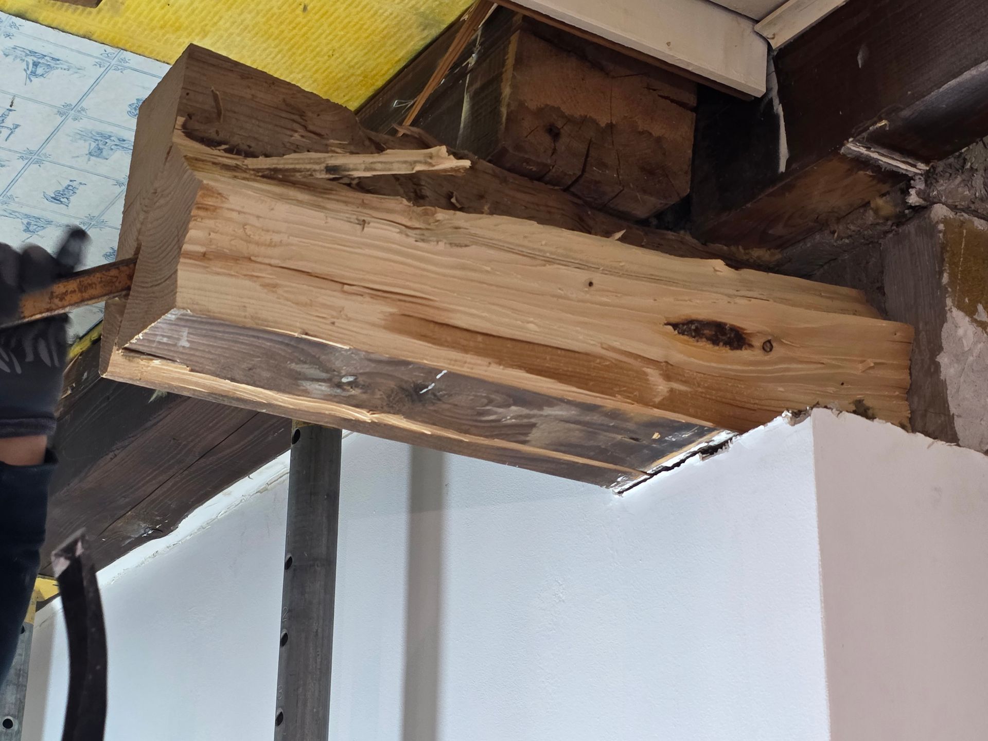 An einem Holzbalken wird gearbeitet; Holz wird zugeschnitten, ein Stützpfosten ist darunter zu sehen.