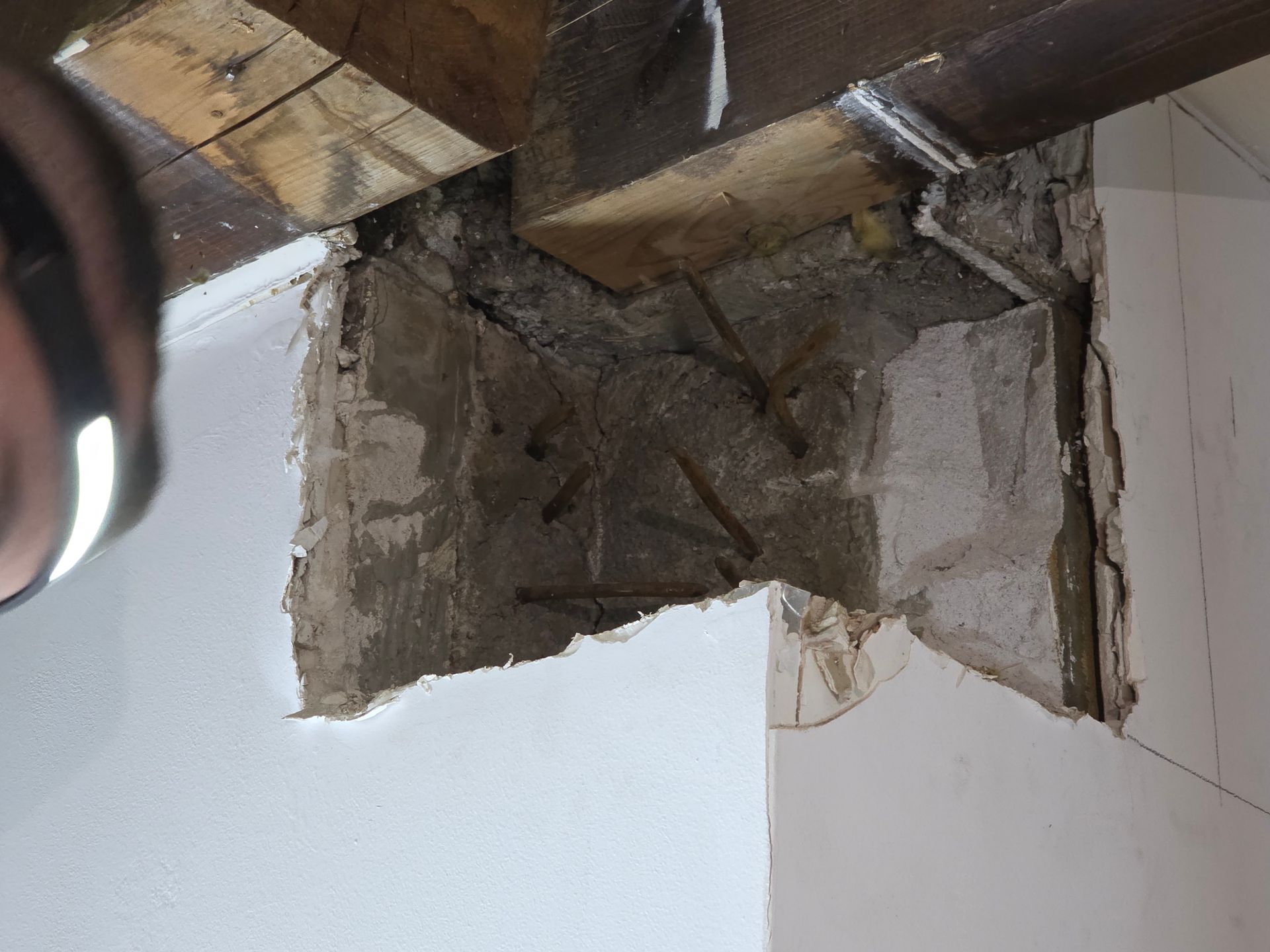 Sichtbarer Stahlbeton und Holzbalken treffen auf eine weiß gestrichene Wand an einer Reparaturstelle.