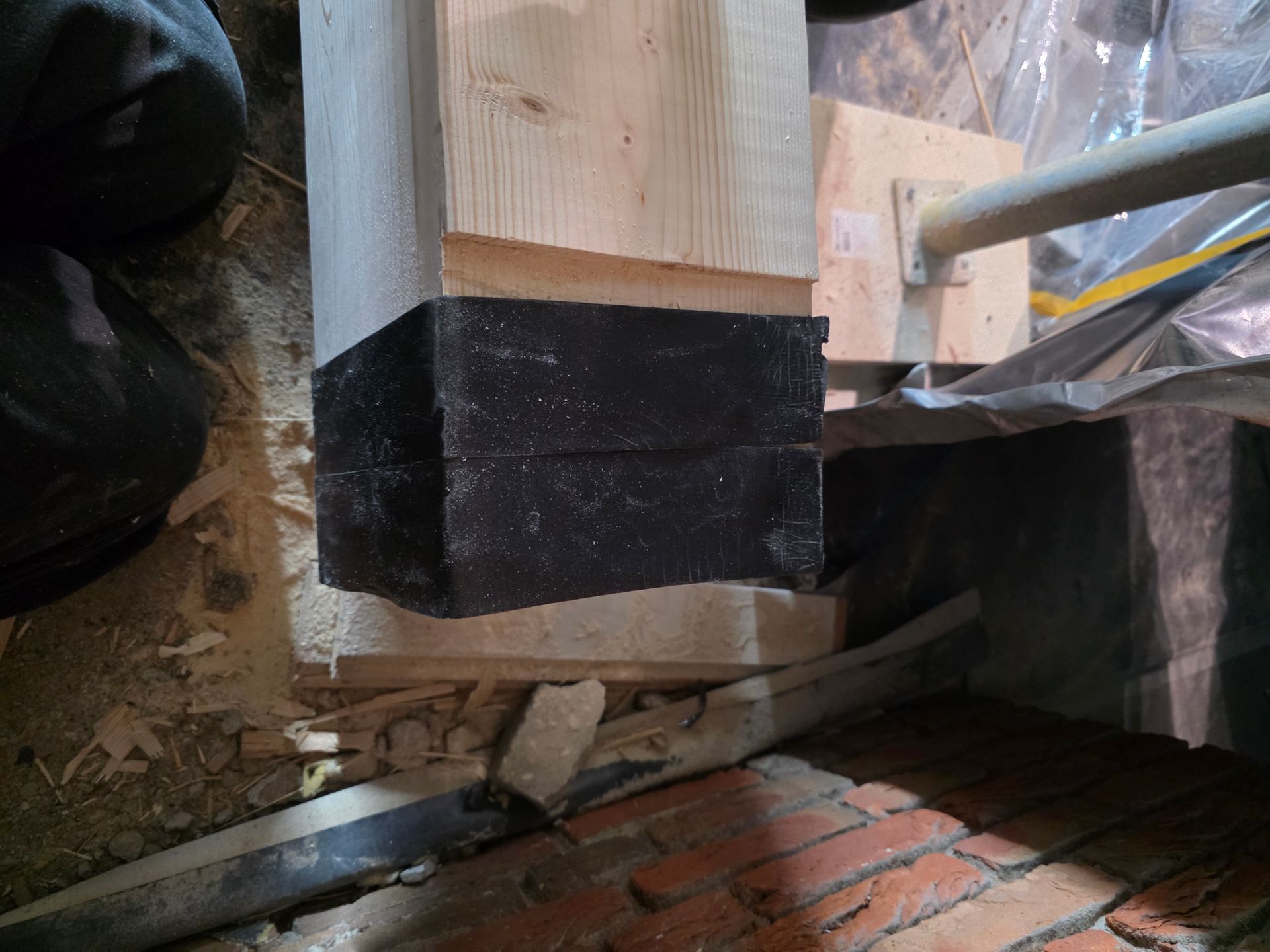 Ein mit schwarzem Band umwickelter Holzpfosten, der auf Ziegeln und Holz ruht, in der Nähe eines Rohrs.