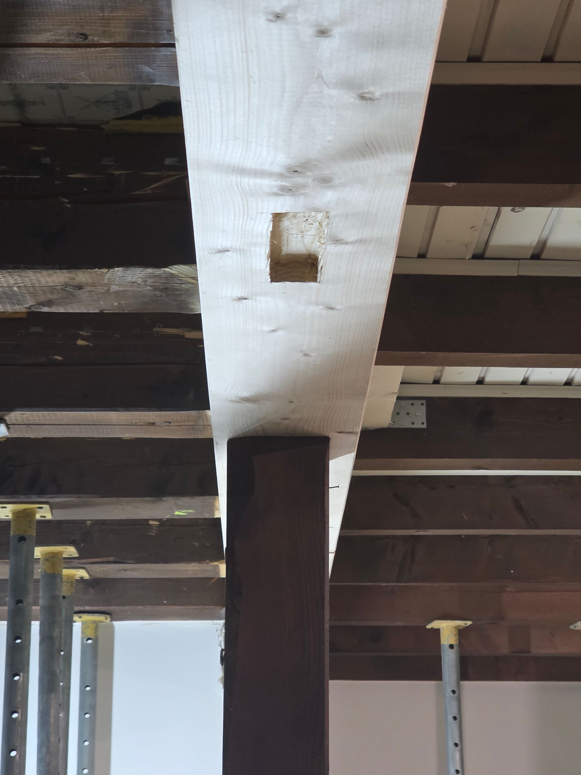 Holzbalken mit Aussparung, getragen von einer dunkelbraunen Säule. Gelbe Stützfüße darunter.