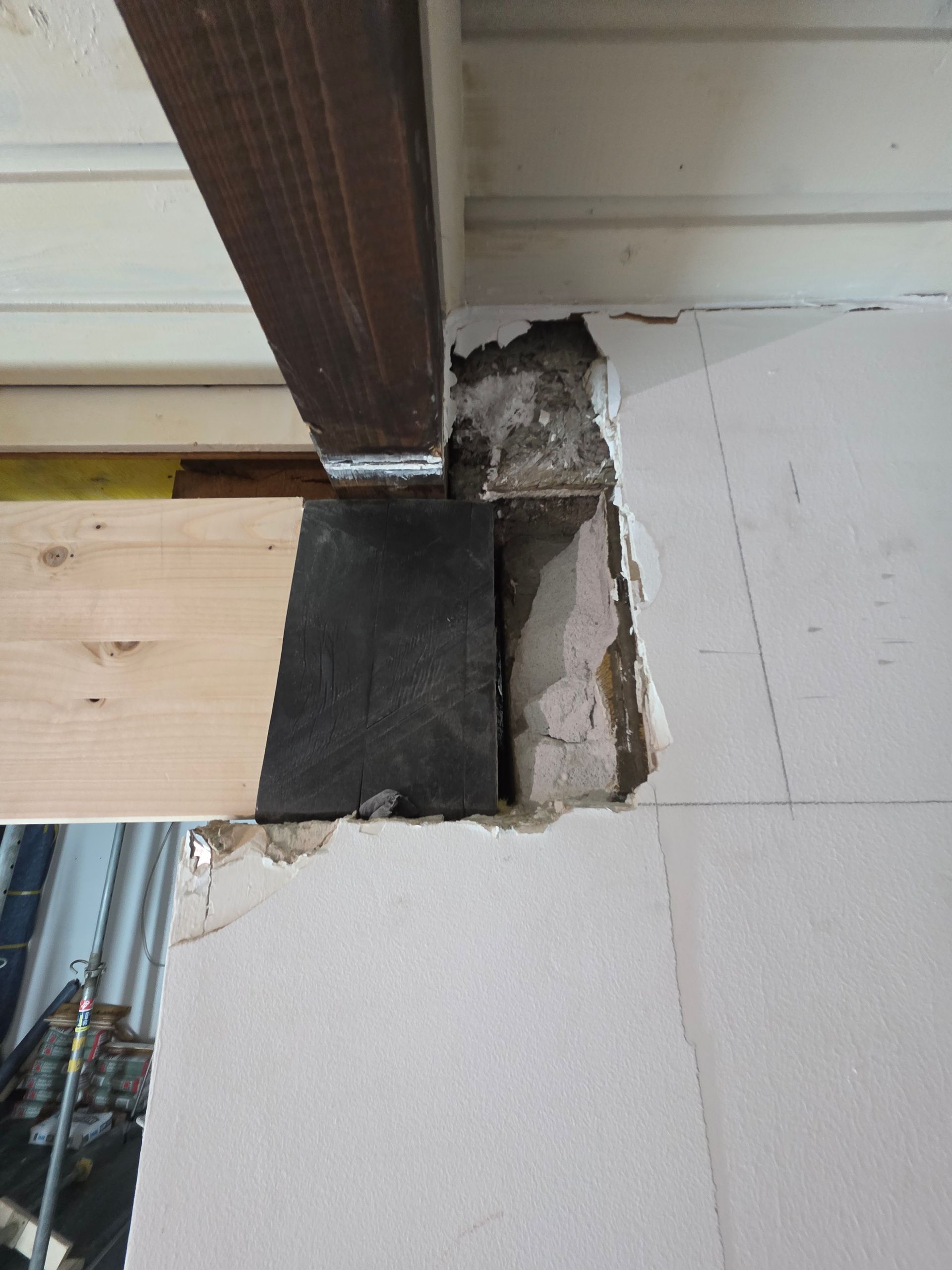 Ein Holzbalken, der von einem dunklen Block getragen wird und teilweise in eine weiße Wand eingelassen ist.