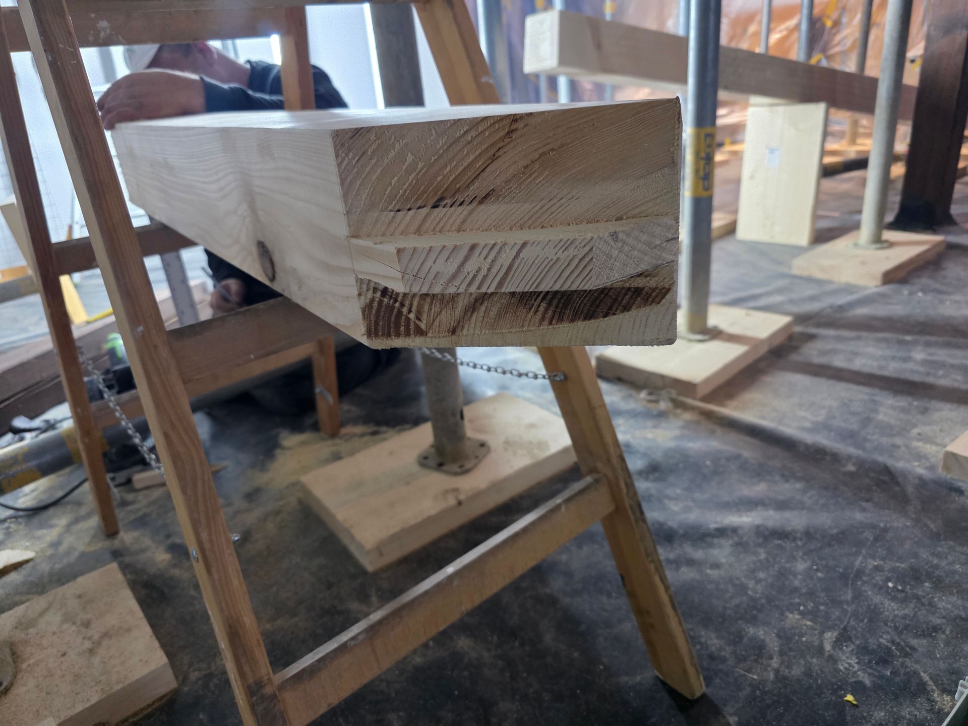 Auf Sägeböcken gelagerter Holzbalken, an dem während der Bauarbeiten gearbeitet wird, Innenaufnahme.