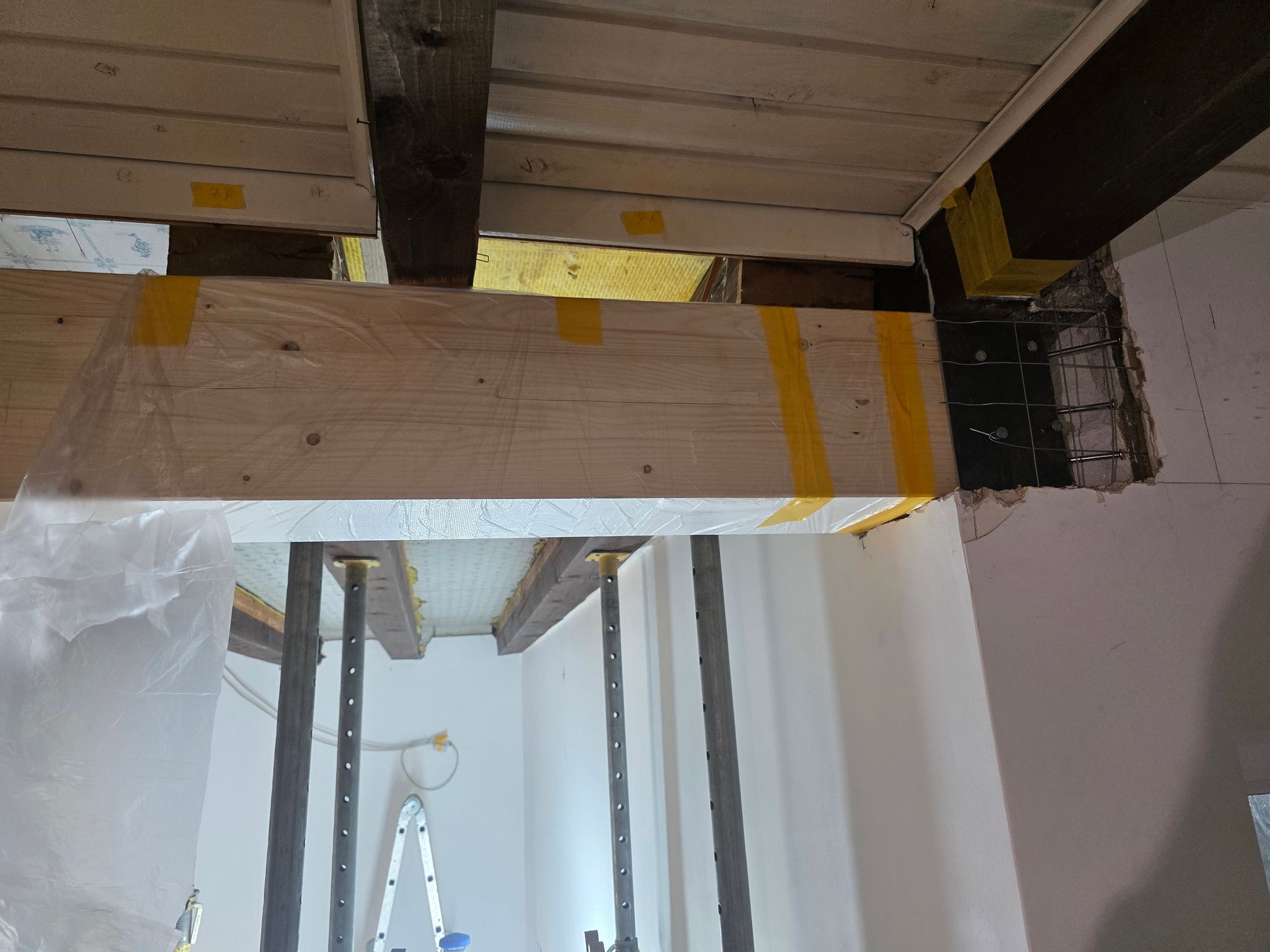 Holzbalkenkonstruktion, mit Klebeband verstärkt, in einem renovierten Raum. Die Stützbalken sind sichtbar.