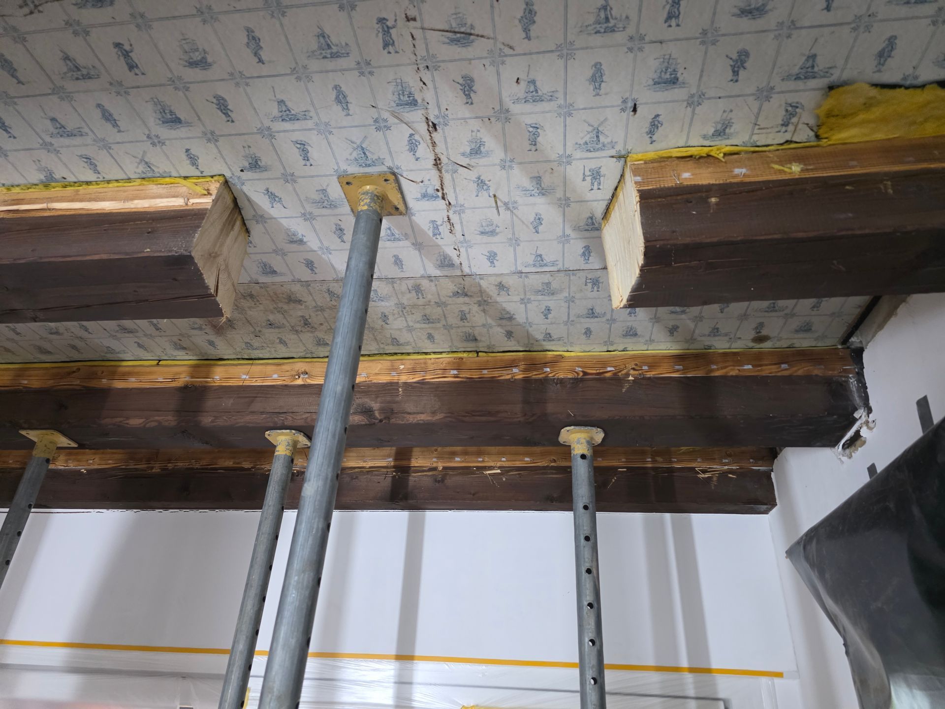 Die Decke wird von Metallstützen getragen und weist freiliegende Balken sowie gemusterte Tapeten auf.