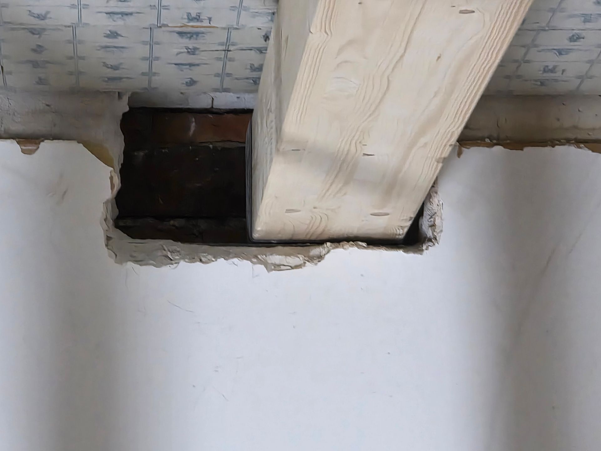 Ein Holzbalken, der durch ein Loch in einer weißen Wand ragt, wird von Ziegelsteinen gestützt.