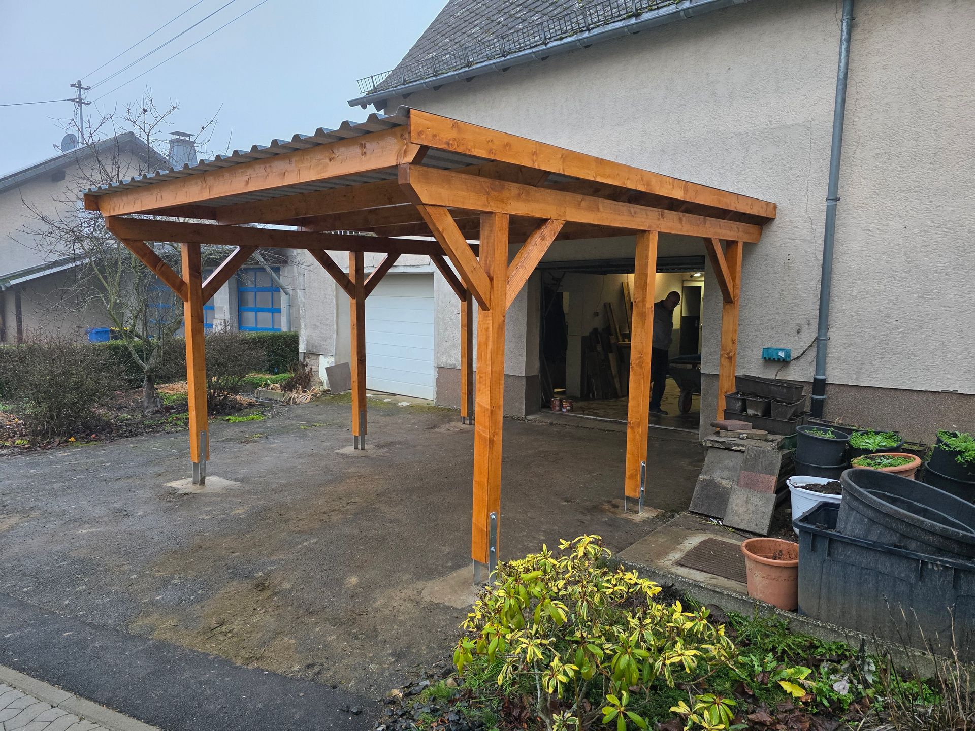 Ein hölzerner Carport ist an ein helles Haus angebaut. Dunkles Dach und Kiesauffahrt.