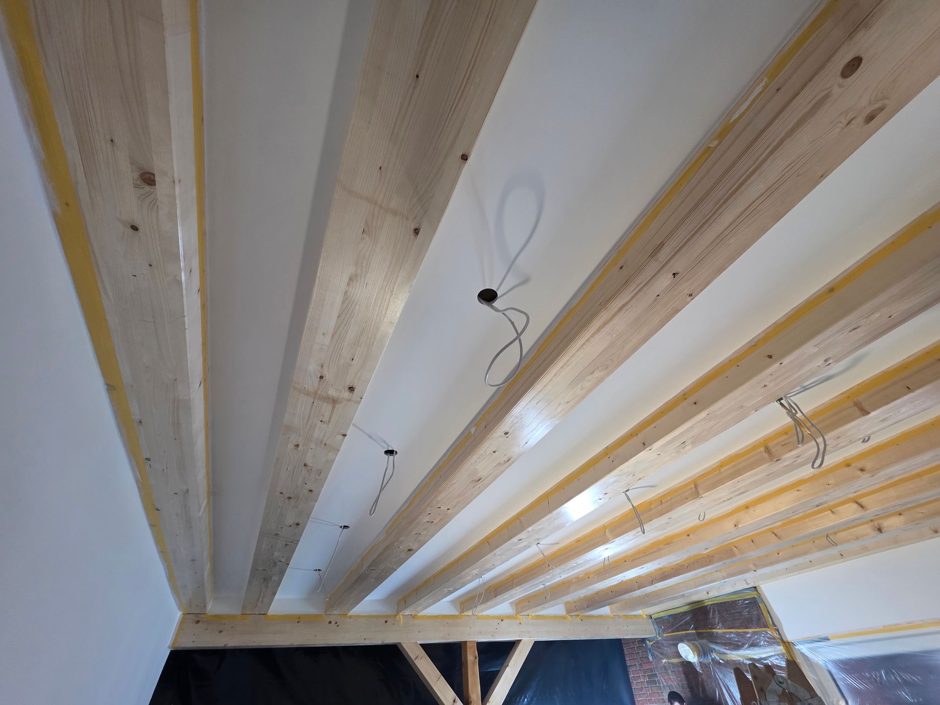 Holzbalken an einer weißen Decke mit freiliegenden Kabeln. Bauarbeiten im Gange.