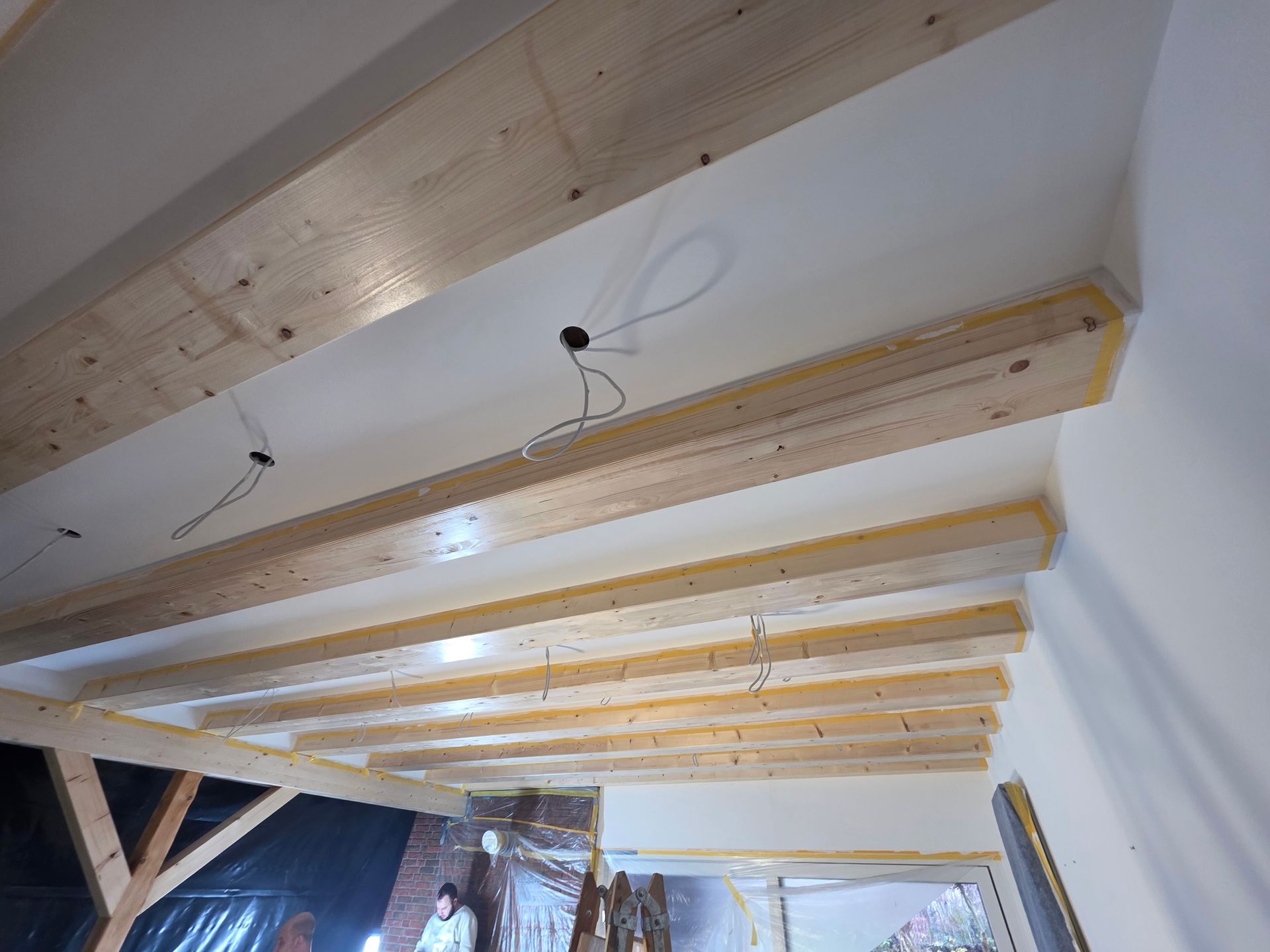 Holzbalken und weiße Decke im Bau mit freiliegenden Kabeln.