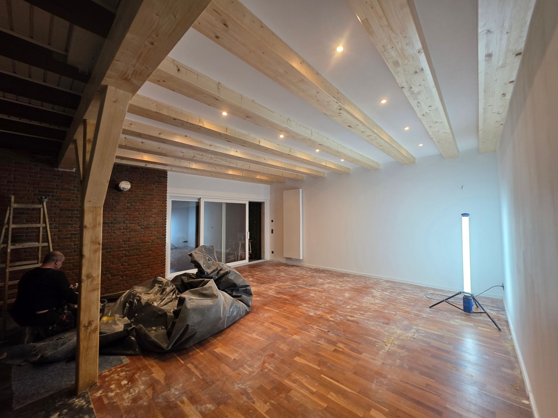 Innenrenovierung im Gange, freiliegende Holzbalken an der Decke, Holzboden mit Bauschutt, ein Mann arbeitet.