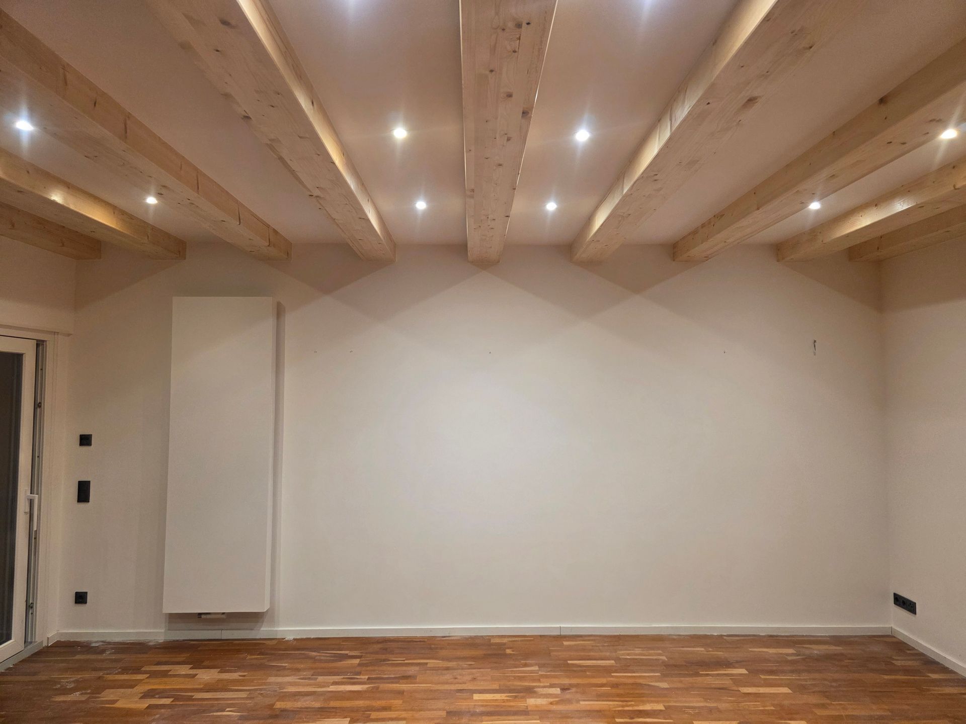 Leeres Zimmer mit Holzbalkendecke, Einbauleuchten, weißen Wänden und Hartholzboden.