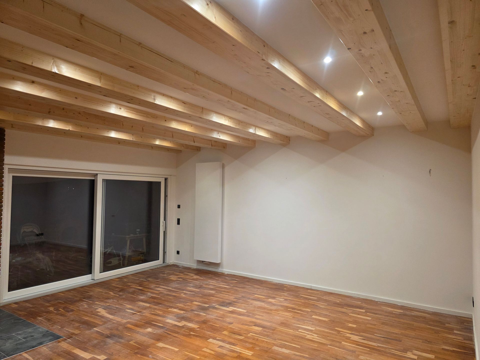 Ein Zimmer mit Holzbalken an der Decke, einer Glasschiebetür und Holzböden.