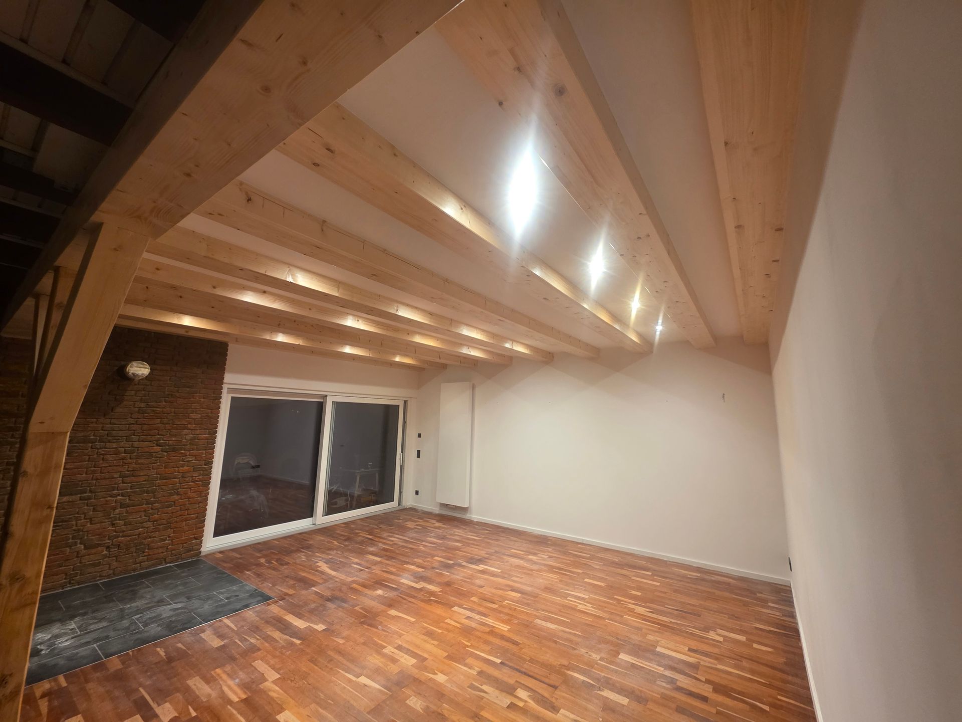 Eine Holzbalkendecke mit Einbaustrahlern in einem Raum mit Holzboden und einer Glasschiebetür.