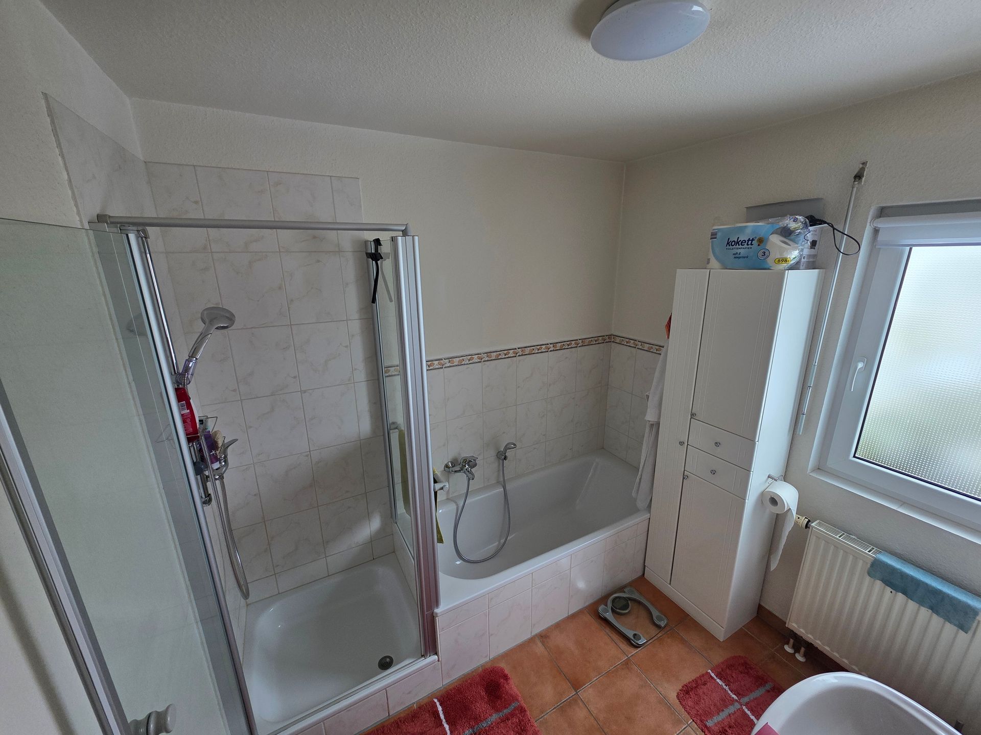 Kleines Badezimmer mit ebenerdiger Dusche, Badewanne, Waschtischunterschrank und Milchglasfenster.