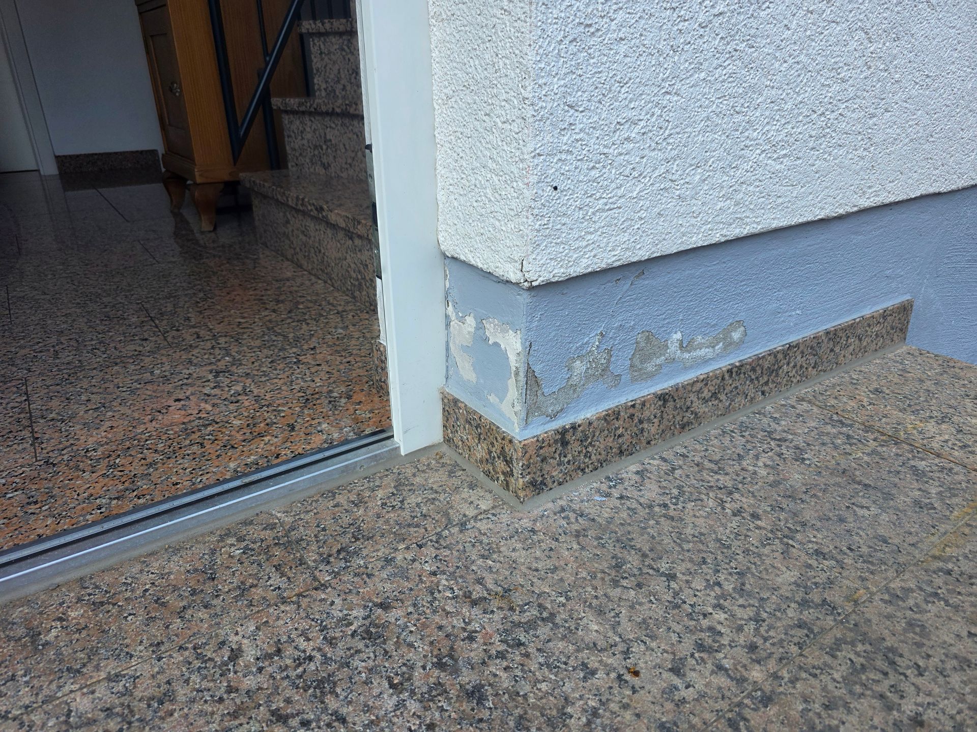 Eingangstür des Gebäudes mit abgeplatzter blauer Farbe und einer niedrigen Schwelle über einem gesprenkelten Steinboden.
