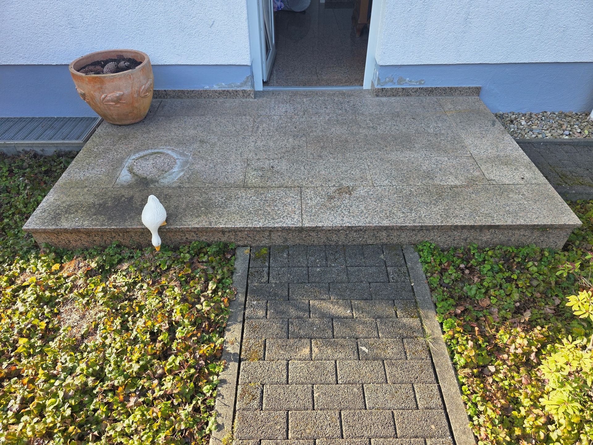 Eine Eingangstreppe aus Beton mit einem Tontopf, einer weißen Vogelfigur und einem Ziegelweg, der zu einer Haustür führt.