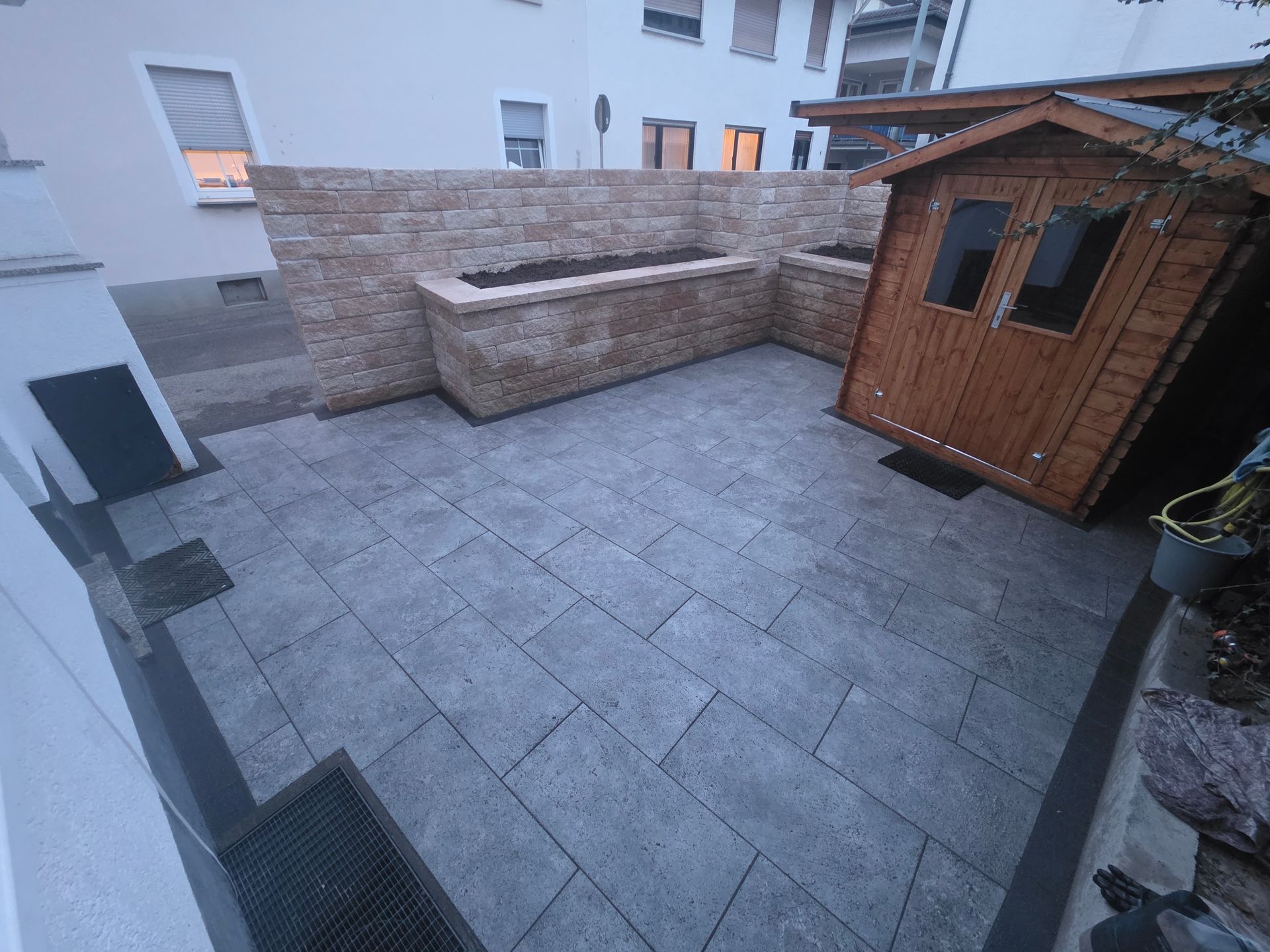 Kleiner, mit Steinen gepflasterter Patio mit einem Holzschuppen, einer eingebauten Bank und Wohnhäusern im Hintergrund