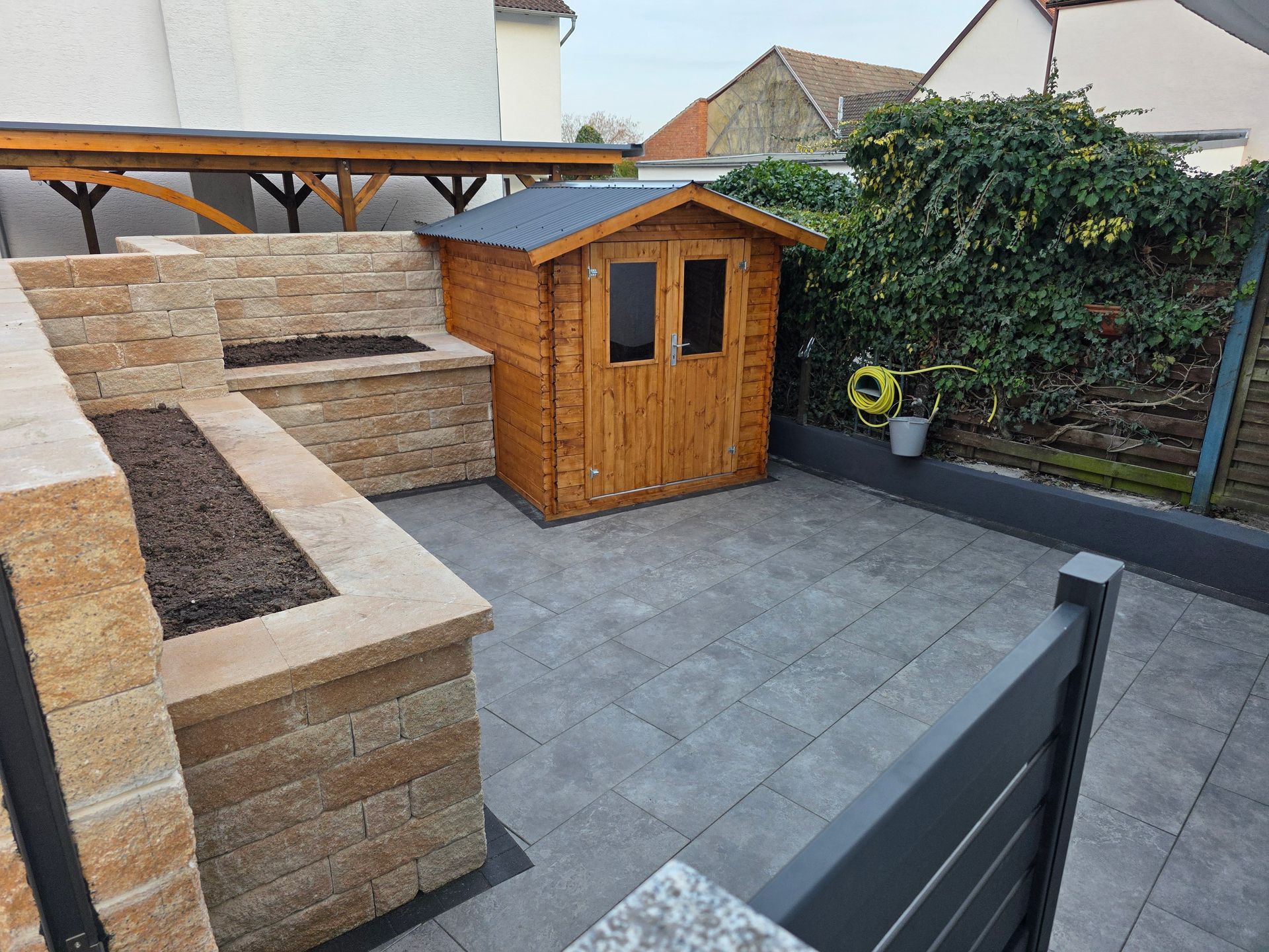 Hinterhofterrasse mit Steinsitzgelegenheiten, Holzschuppen und grauen Pflastersteinen.