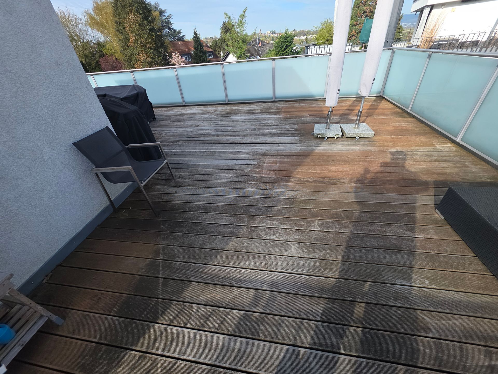 Holzterrasse auf dem Dach mit Stühlen, Grill und Milchglasgeländer im hellen Sonnenlicht