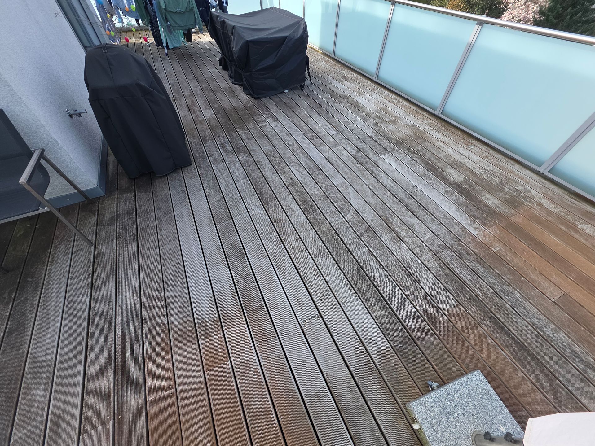 Nasse Holzterrasse mit zwei überdachten Stühlen und Milchglasgeländer unter bedecktem Himmel