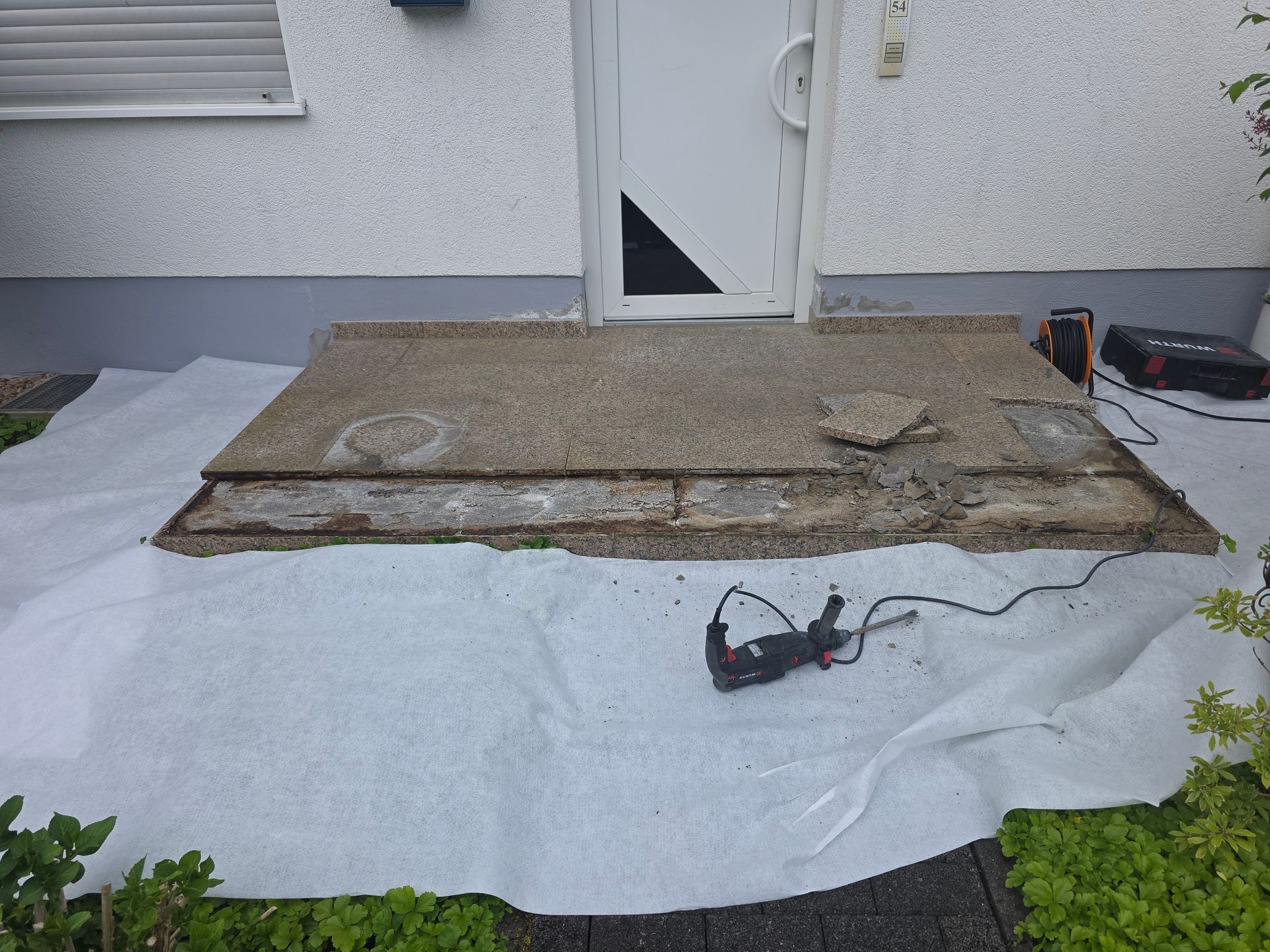 Ausrüstung zur Reparatur einer Außenterrassentreppe mit einer freistehenden Betonplatte, einer Plane und einem Elektrowerkzeug.