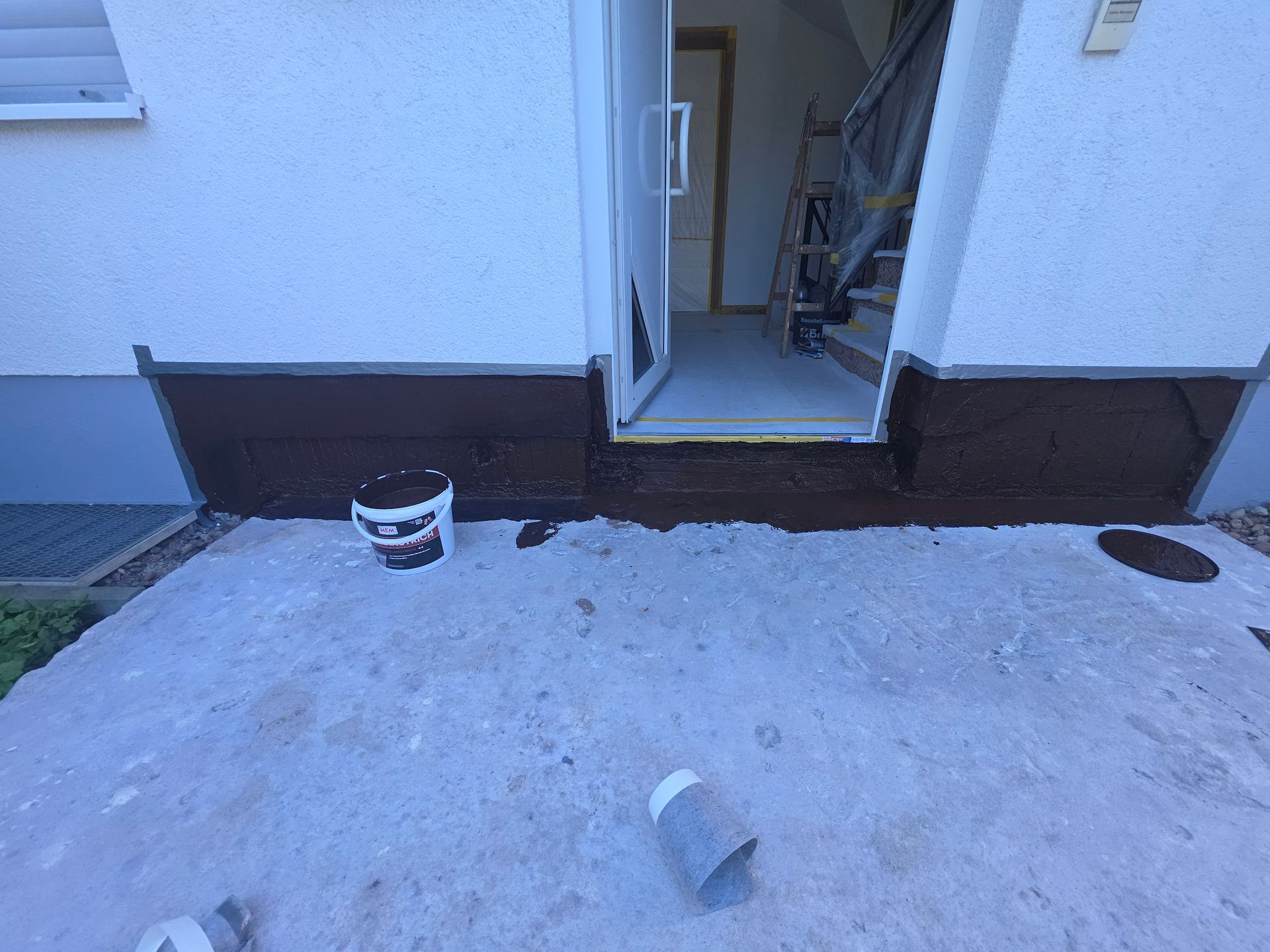 Außentür mit einem Eimer, einem kleinen Rohr und einer Betonplatte neben einem Haus.