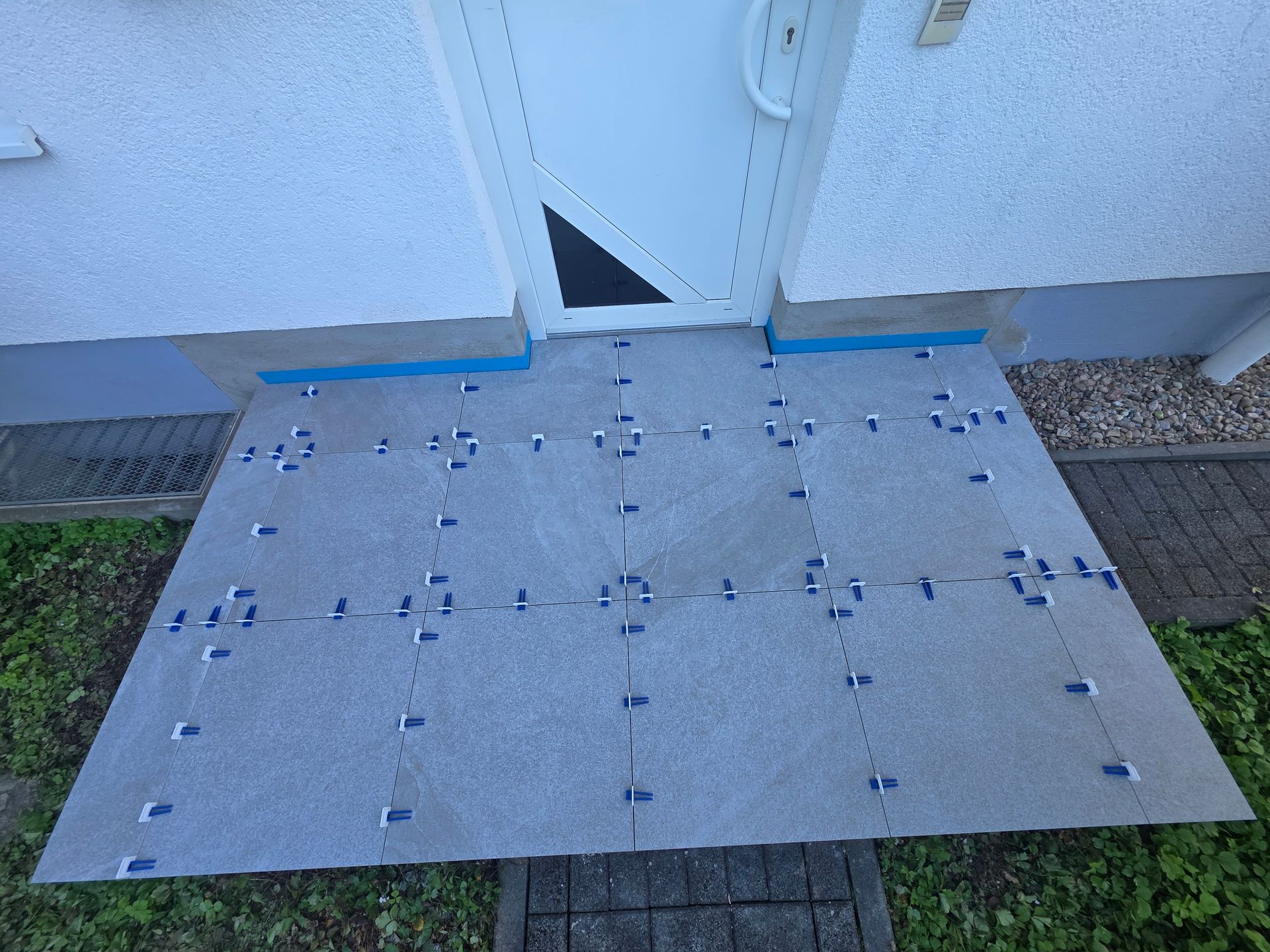 Barrierefreie Metallrampe an einem Türrahmen mit blauen Kantenstreifen und grauer, strukturierter Oberfläche.