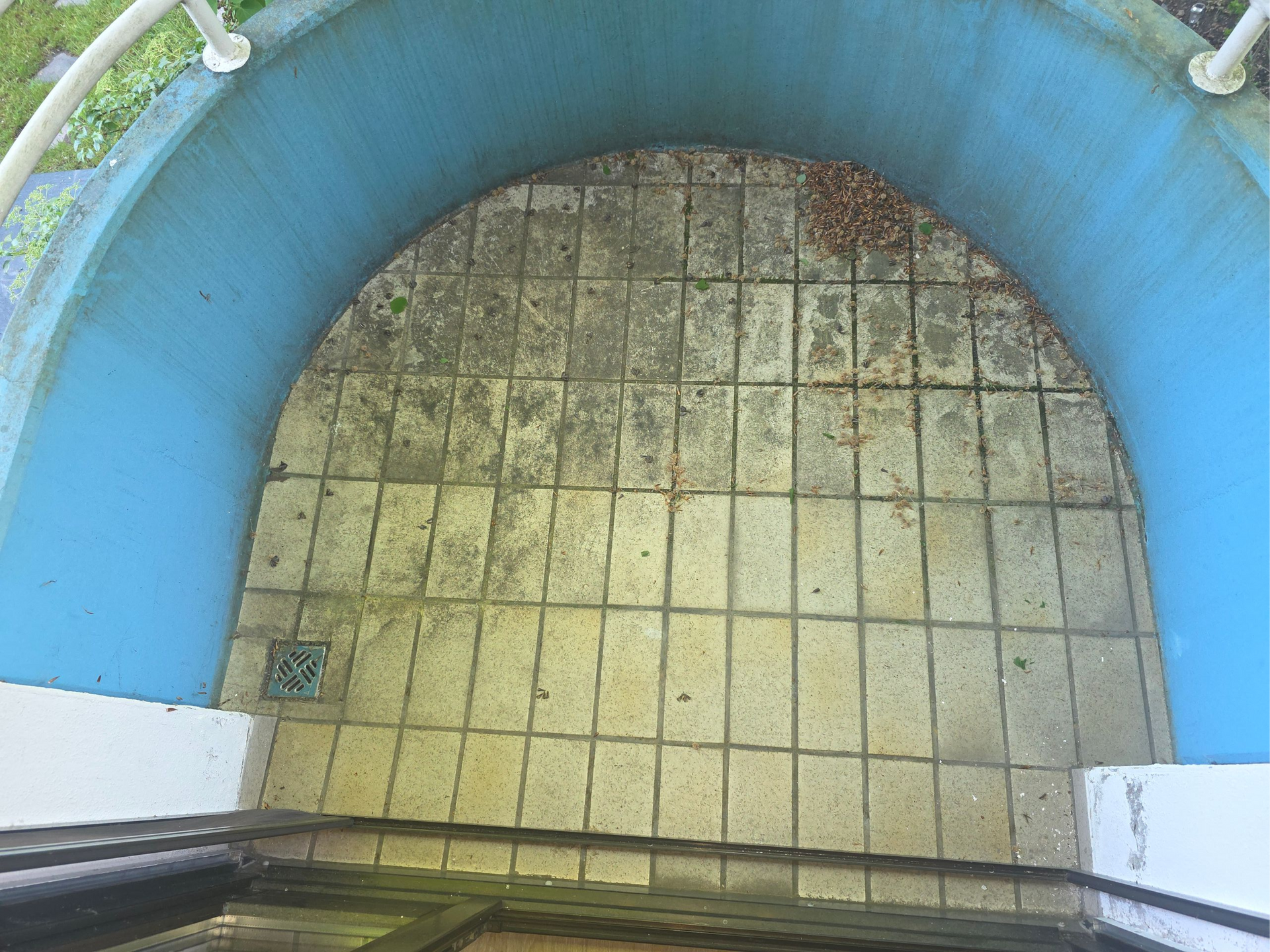 Blick hinunter in ein blau umrandetes rundes Becken oder einen Brunnen mit gefliestem Boden und Abfluss.