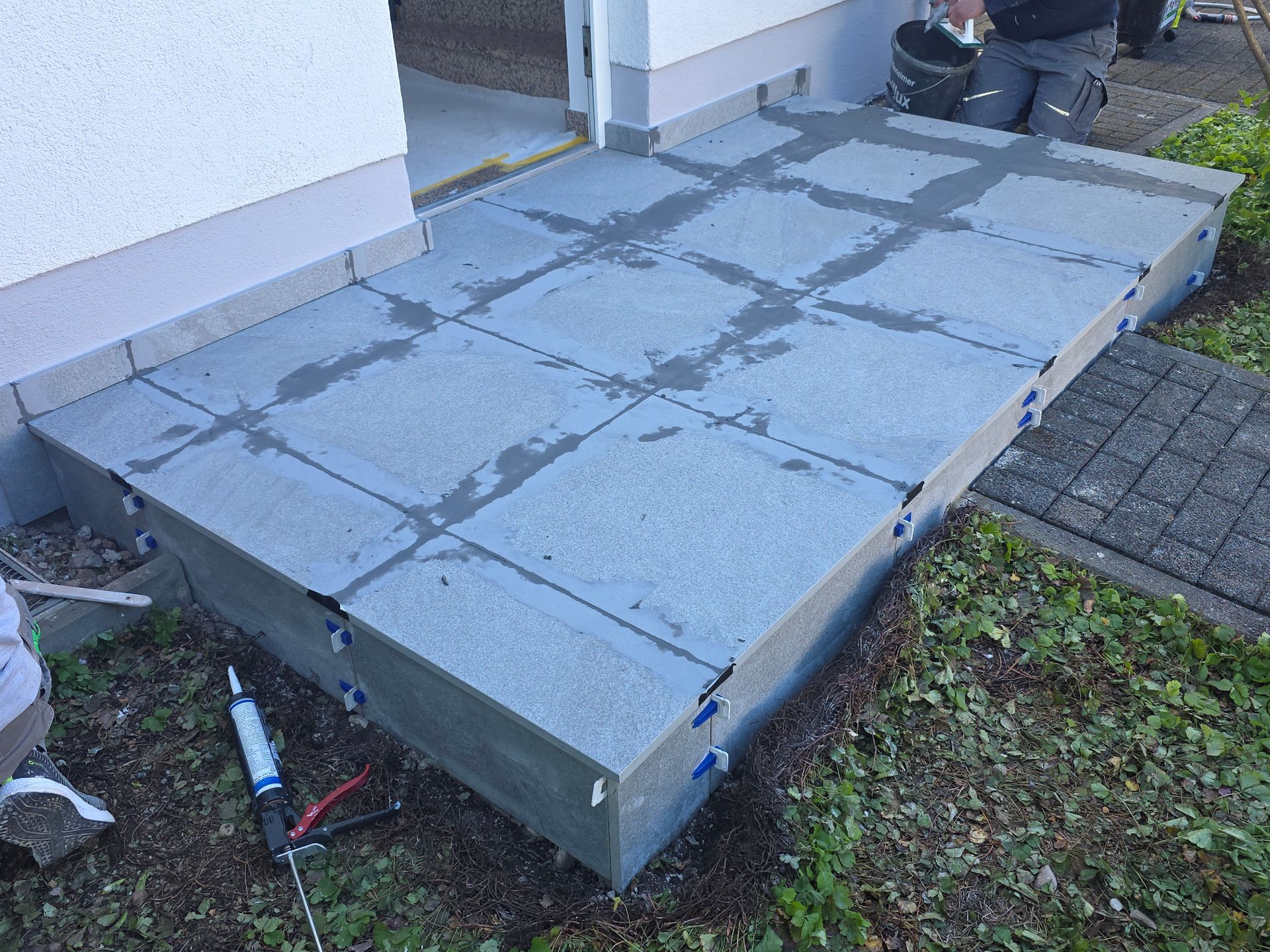 Erhöhte Terrassenstufen aus Beton neben einem Haus, mit gefliestem Gehweg und Garteneinfassung.