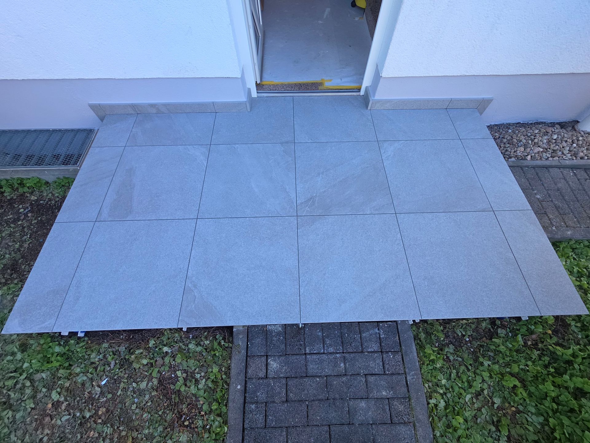 Ein kleiner Backsteinweg führt zu einer Tür mit grauen Pflastersteinen und Rasenkanten.