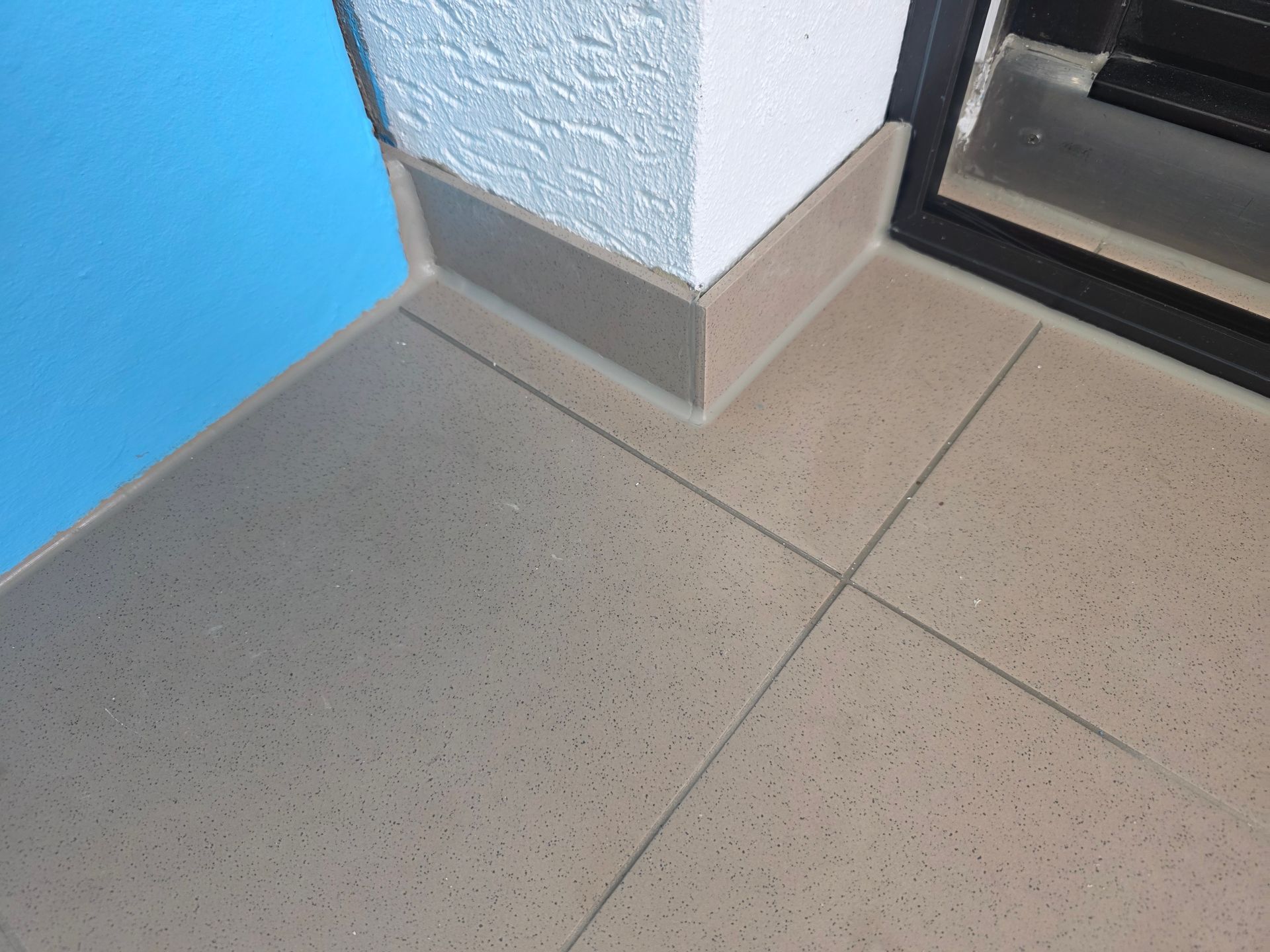 Ecke eines gefliesten Bodens neben einer blauen Wand und einem Türrahmen.