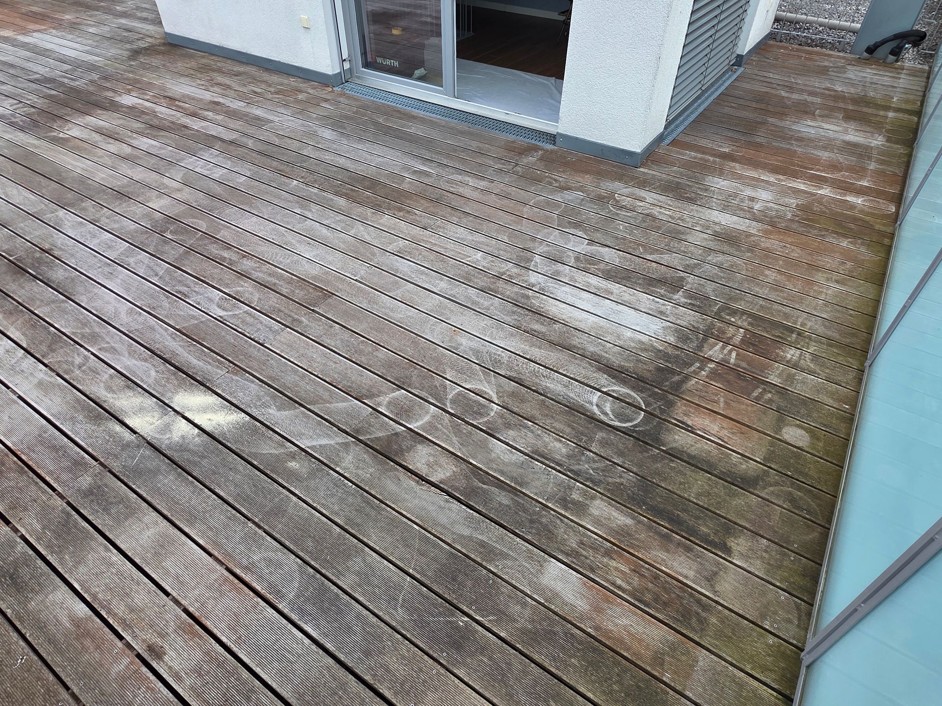 Verwitterte Holzdielen mit Schneeflecken neben einem Haus.