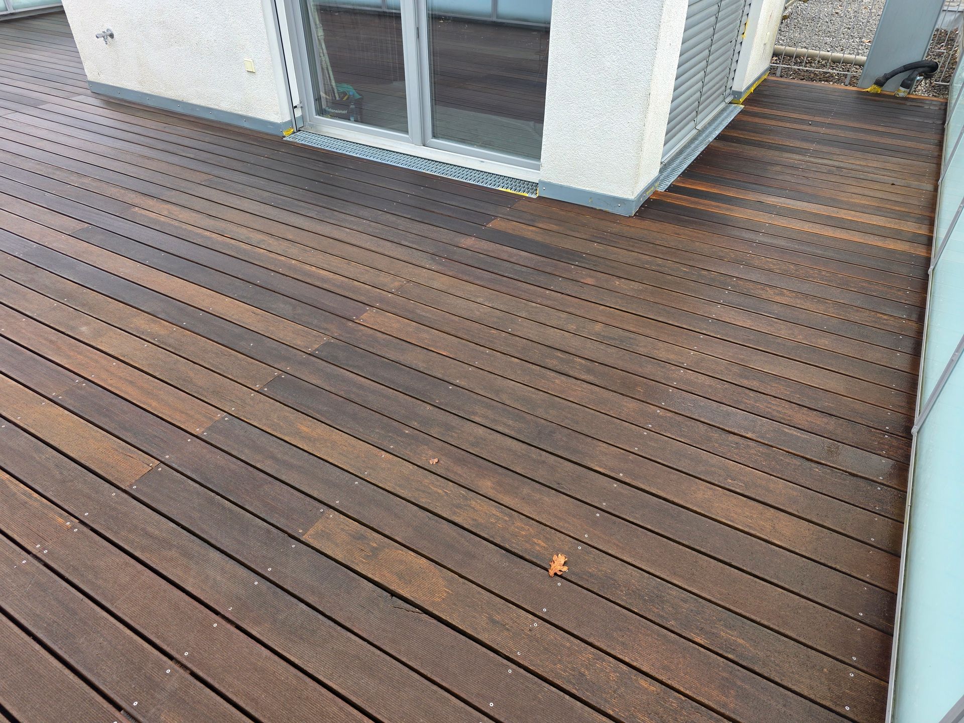 Holzterrasse neben einem weißen Haus mit Glasschiebetüren, von oben betrachtet.